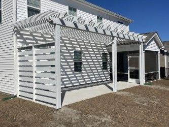 White pergola with horizontal slat privacy screen on a concrete patio next to a house.