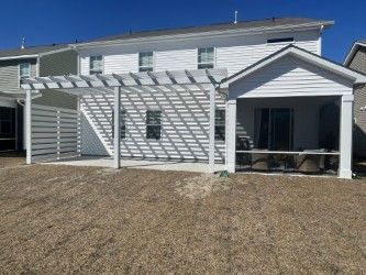 White pergola attached to a white house with a covered patio.