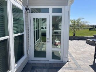 White door with glass panels on a patio, adjacent to a large window. Sunny outdoors.