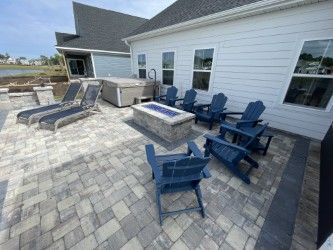 Patio with blue chairs around a fire pit, lounge chairs, and a hot tub next to a light blue house.