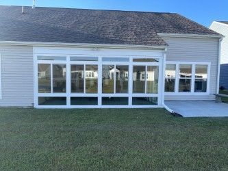 Sunroom addition with many white-framed windows, attached to a house with gray siding and a dark roof.