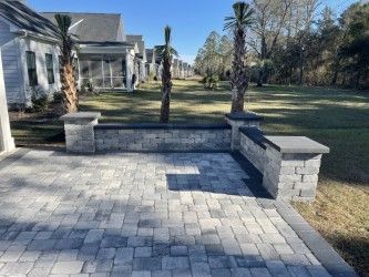 Paver patio with a low stone wall and capped columns; palm trees in the background.