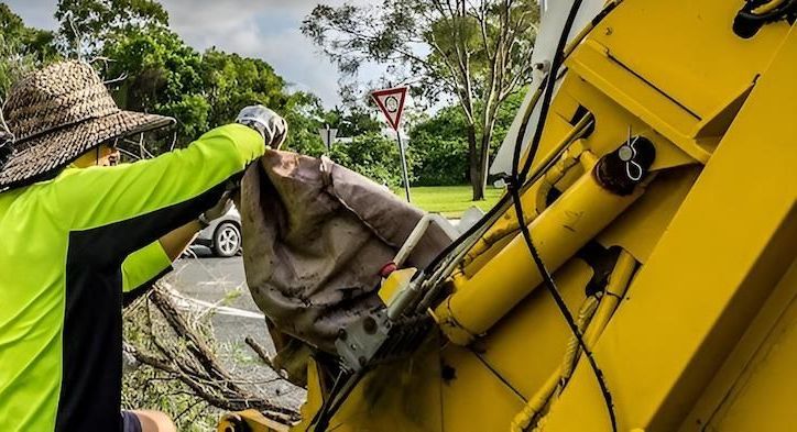 Person in Neon Shirt Empties a Sack Into a Yellow Garbage Truck — Bobs Bags & Bins in Mackay, QLD