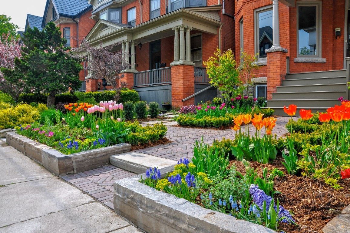 Brick house with vibrant flowerbeds and steps leading to a porch.