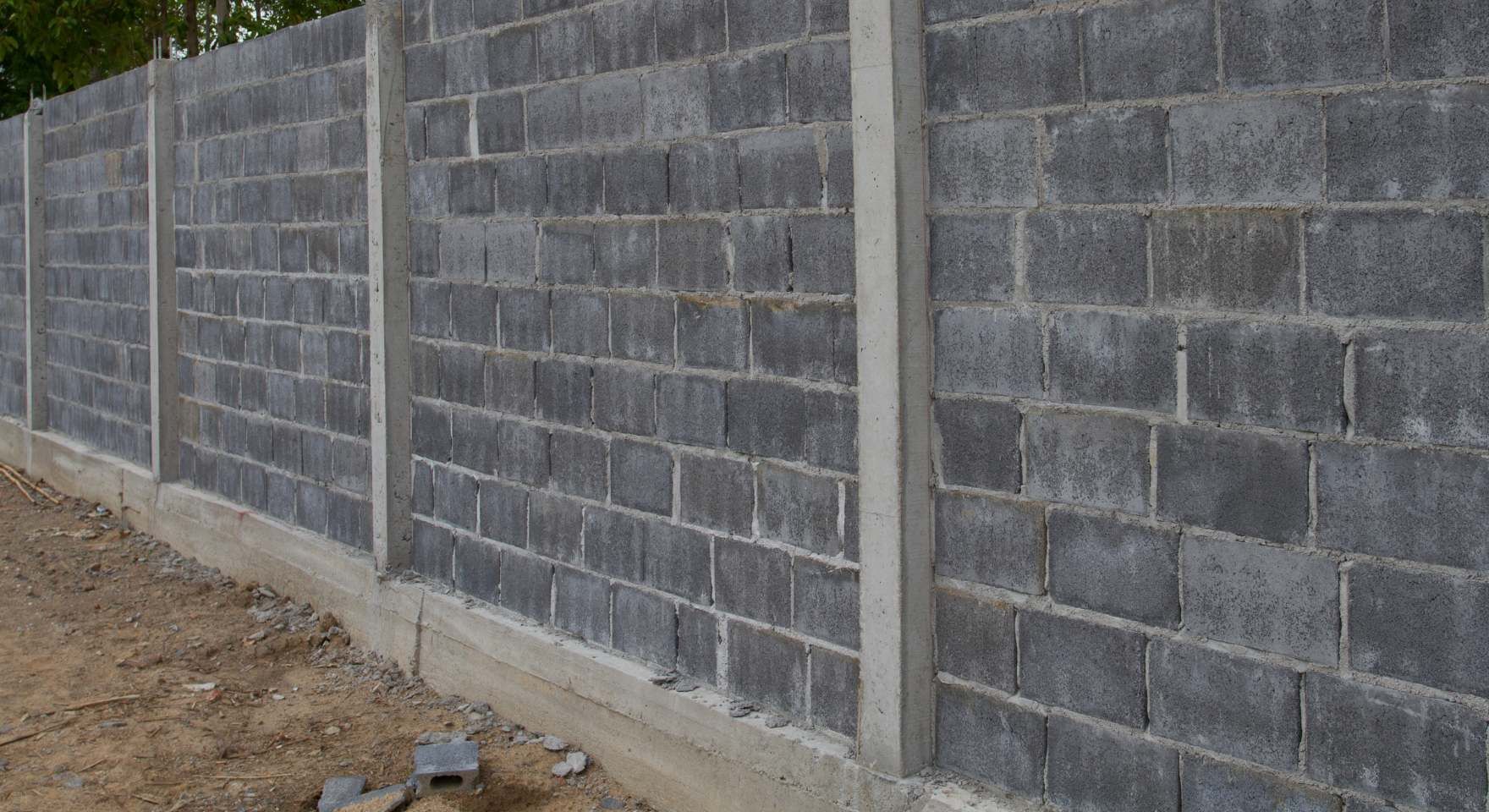 “Dark concrete block privacy wall with vertical support columns along a dirt edge during a block and retaining wall service in Santa Ana, CA”