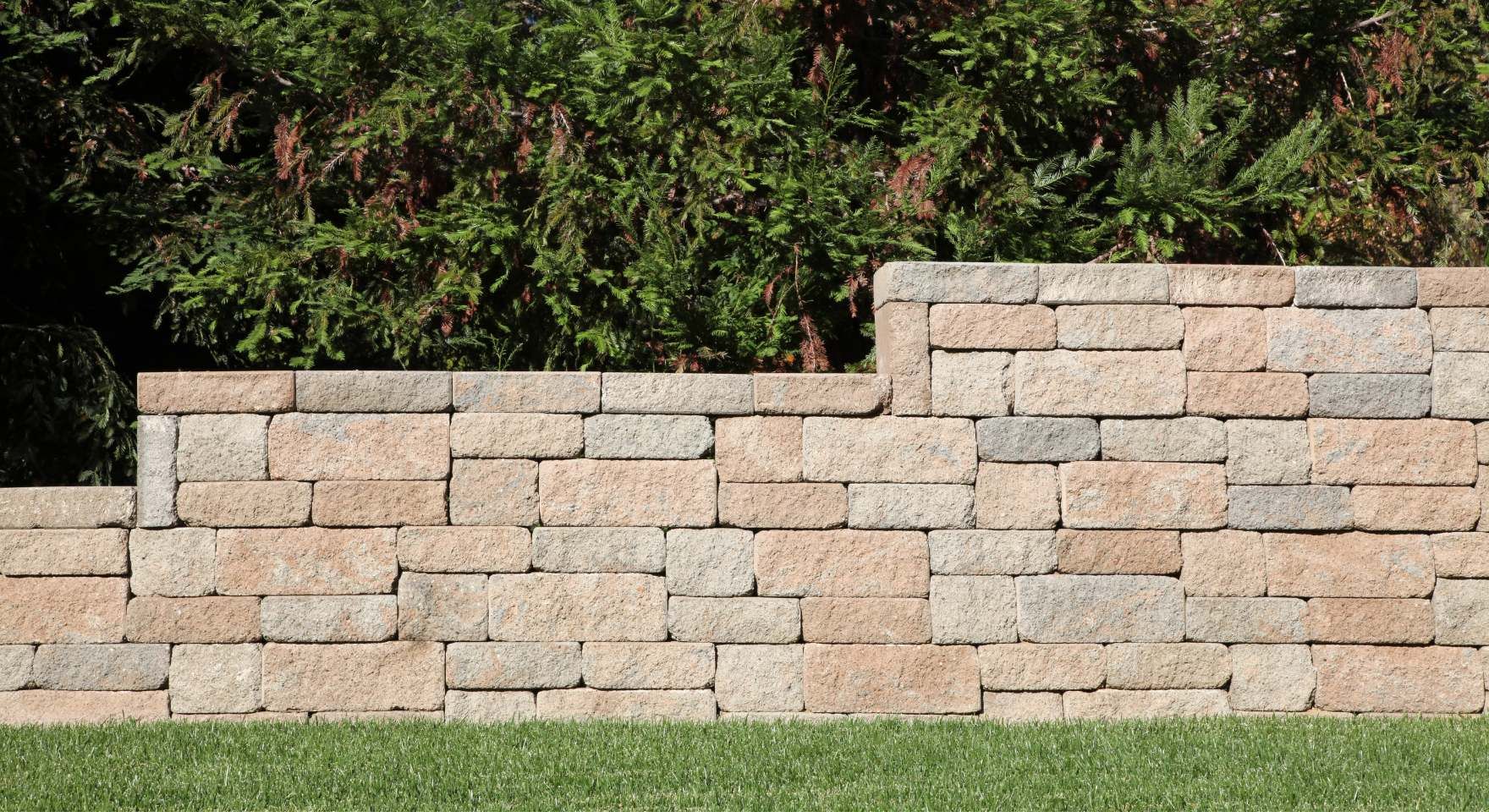 Short concrete block retaining wall holding back a landscaped slope with greenery during a block and retaining wall service in Santa Ana, CA