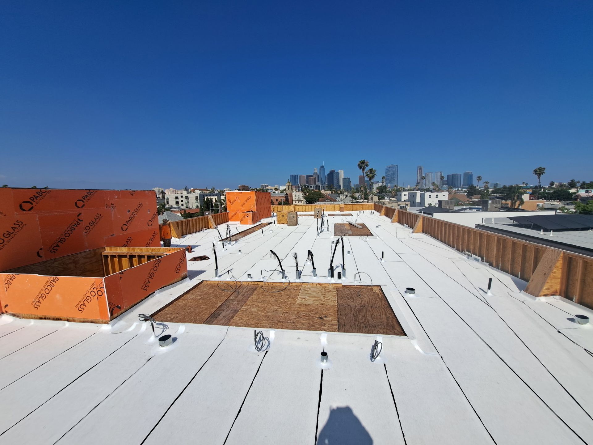 Rooftop with white coating, orange structures, and distant city skyline under a clear blue sky