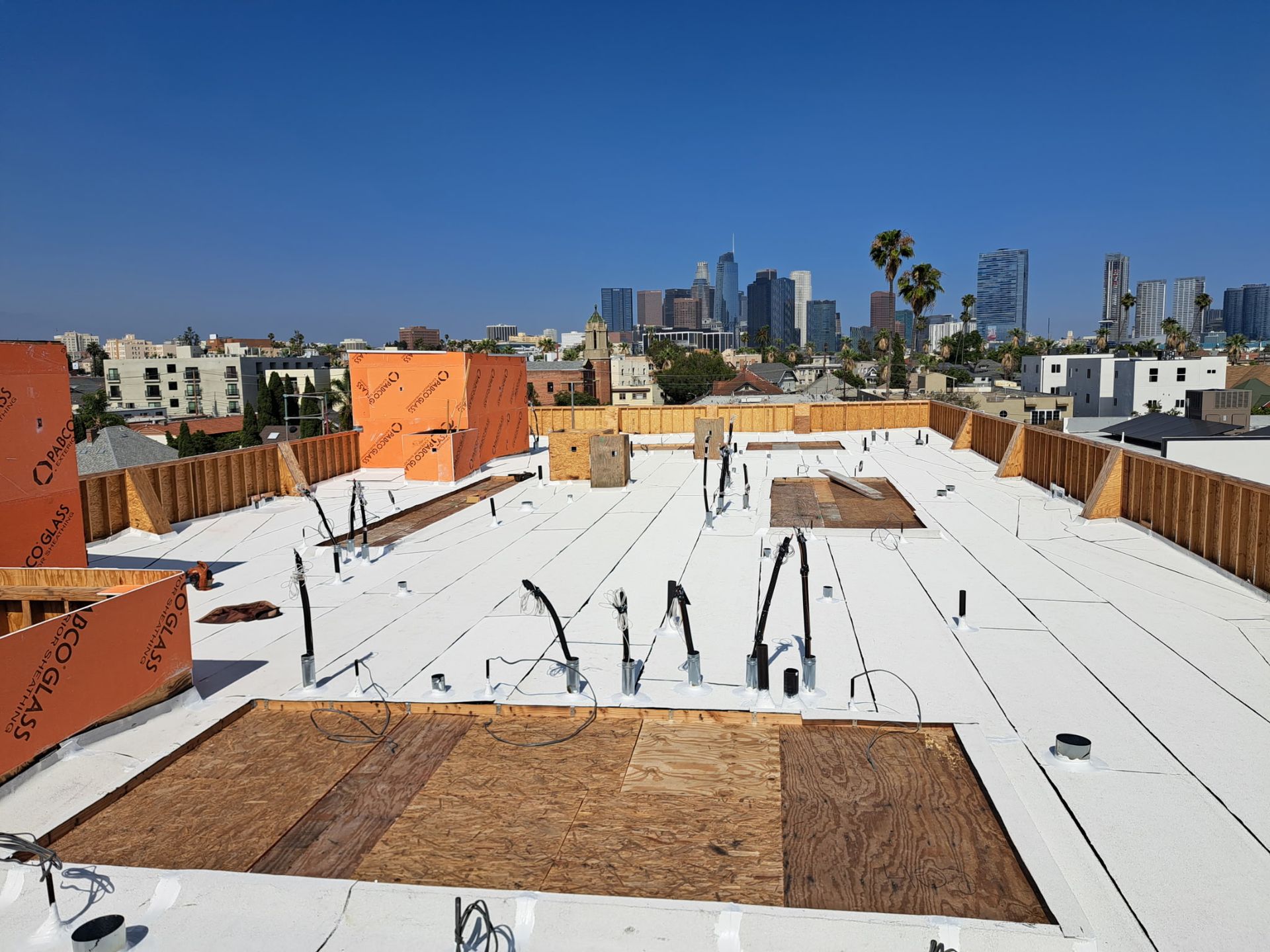 Roof under construction with workers, white roofing membrane, and city skyline in the background