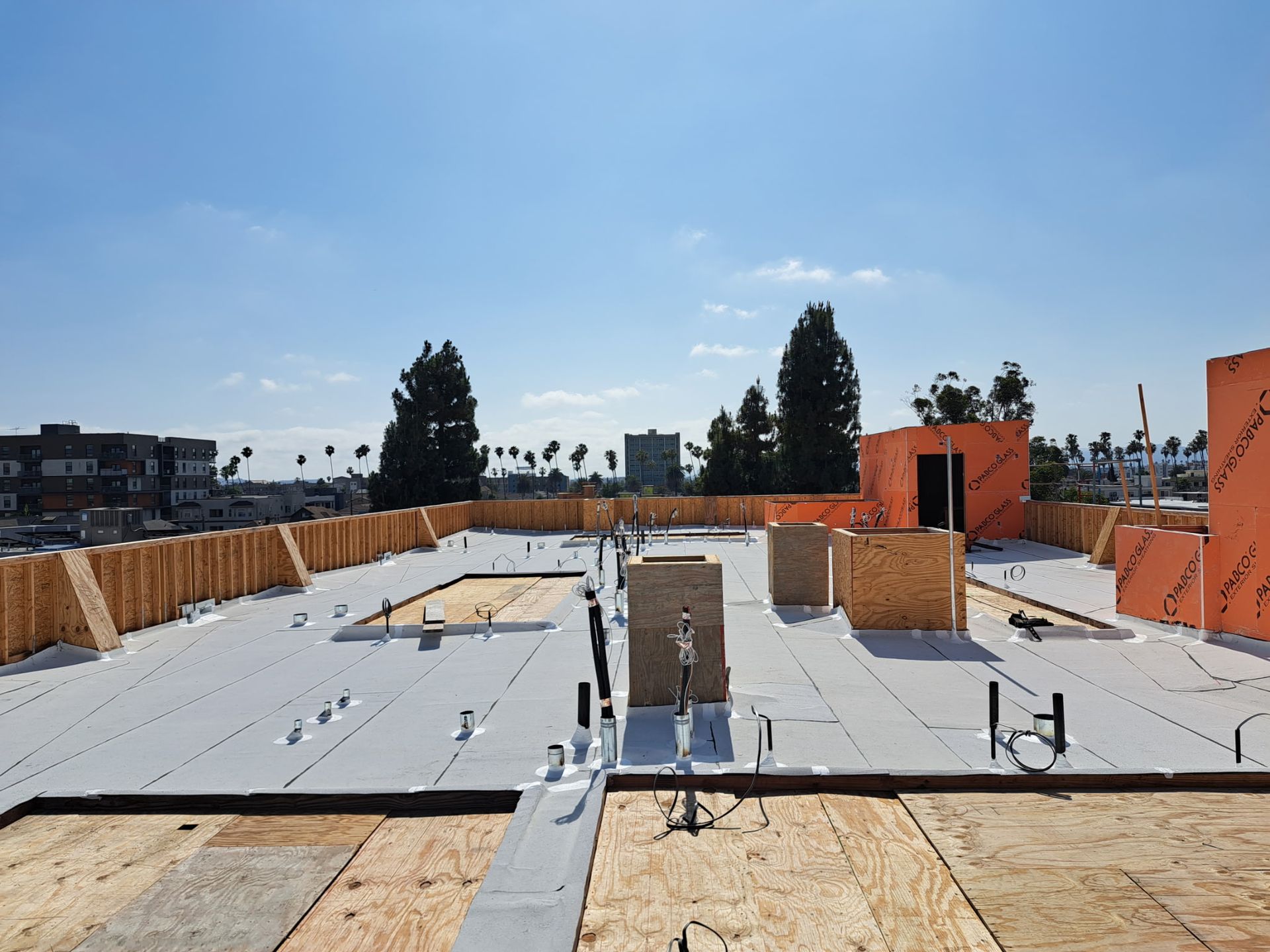 Rooftop construction site with white waterproofing sheets, brick structures, and blue sky.