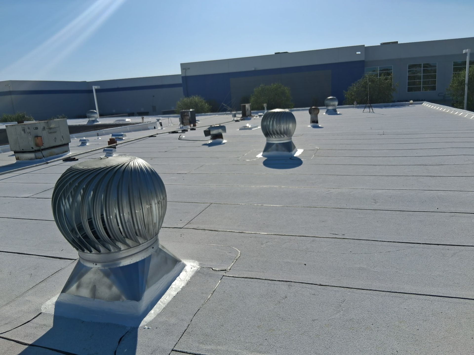 Rooftop with several silver vent turbines on a flat gray roof under a clear blue sky