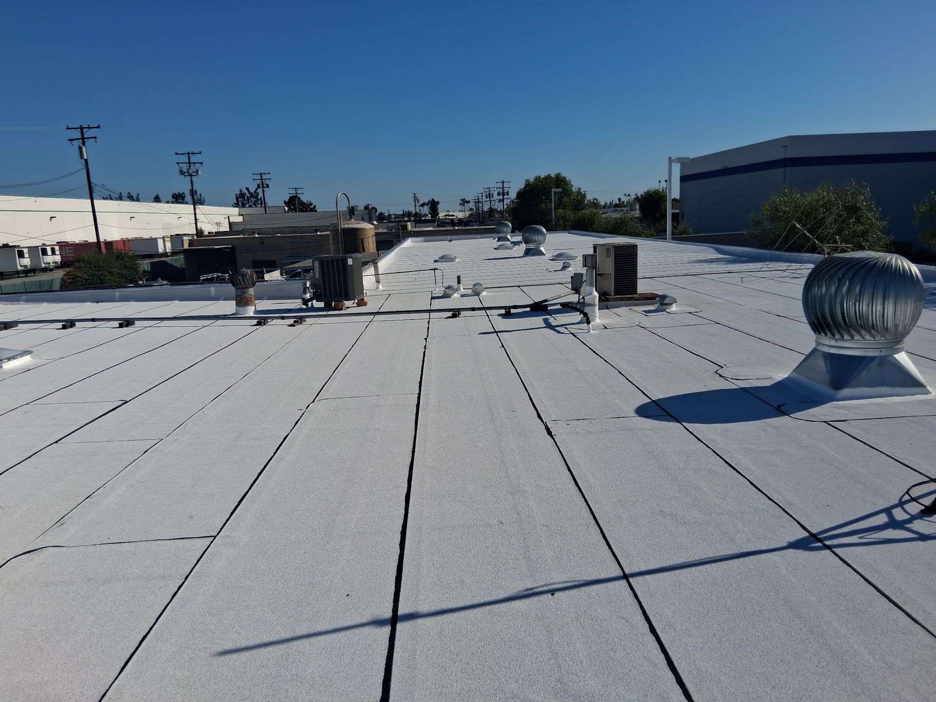Flat white rooftop with vents and utility equipment under a clear blue sky