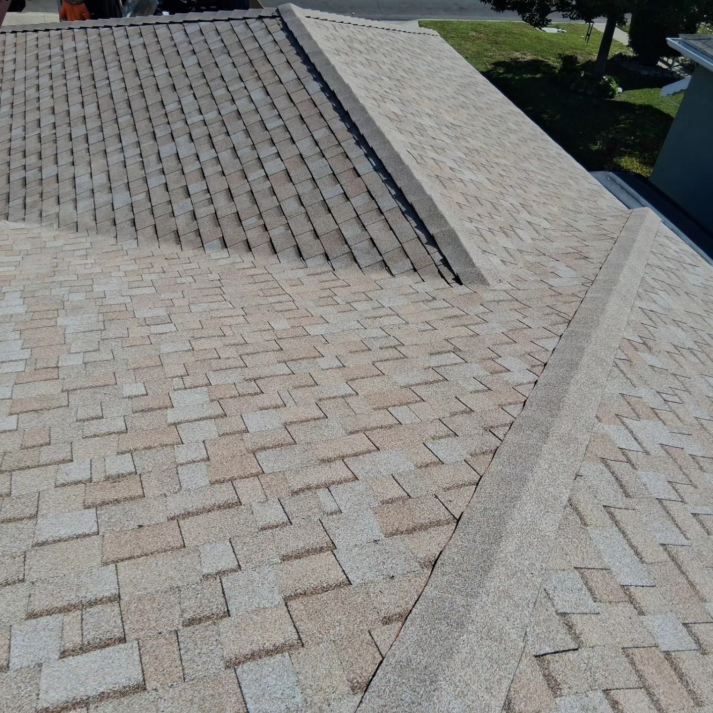 Roof with gray asphalt shingles and a light-colored ridge on a sunny day