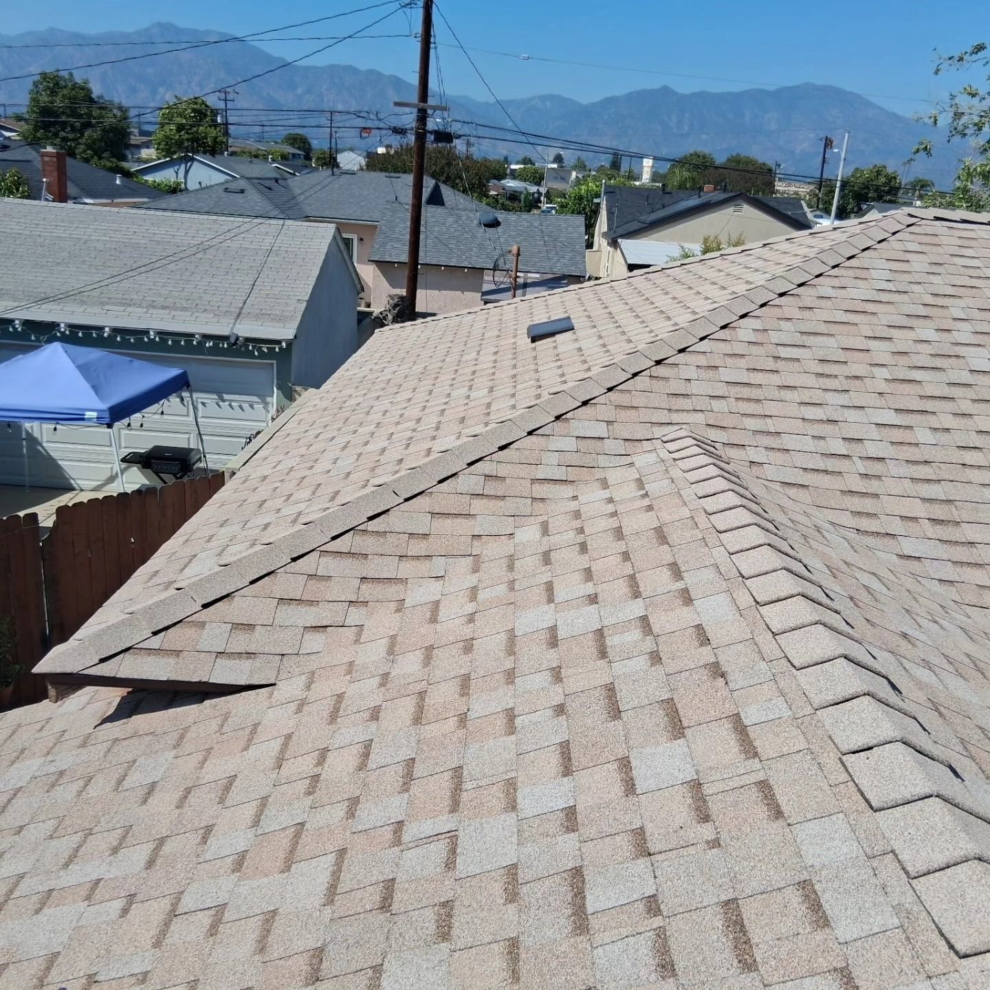 Rooftop with tan shingles overlooking houses, mountains, and a clear blue sky