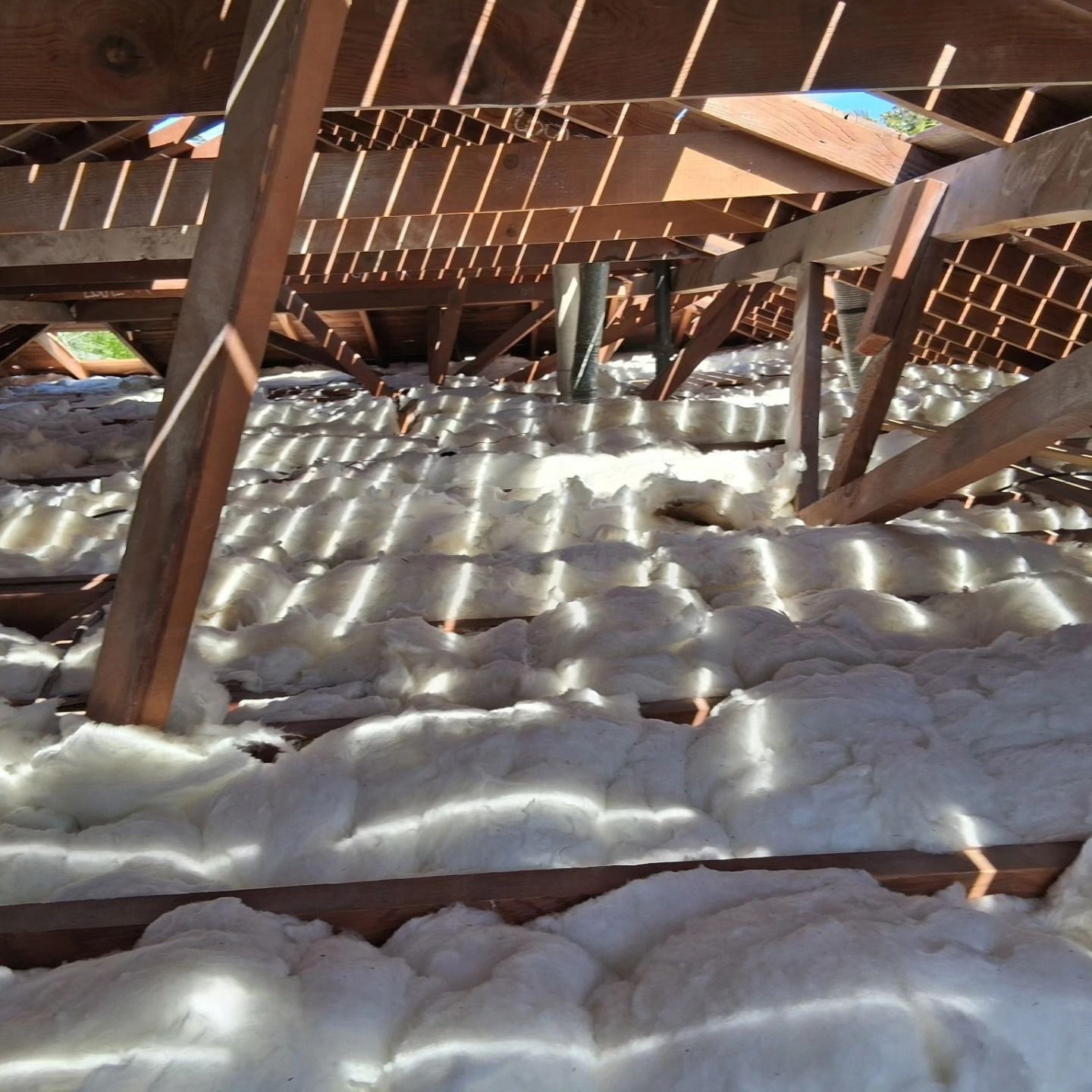 Insulated attic roof with exposed wooden rafters and sunlight filtering through the slats