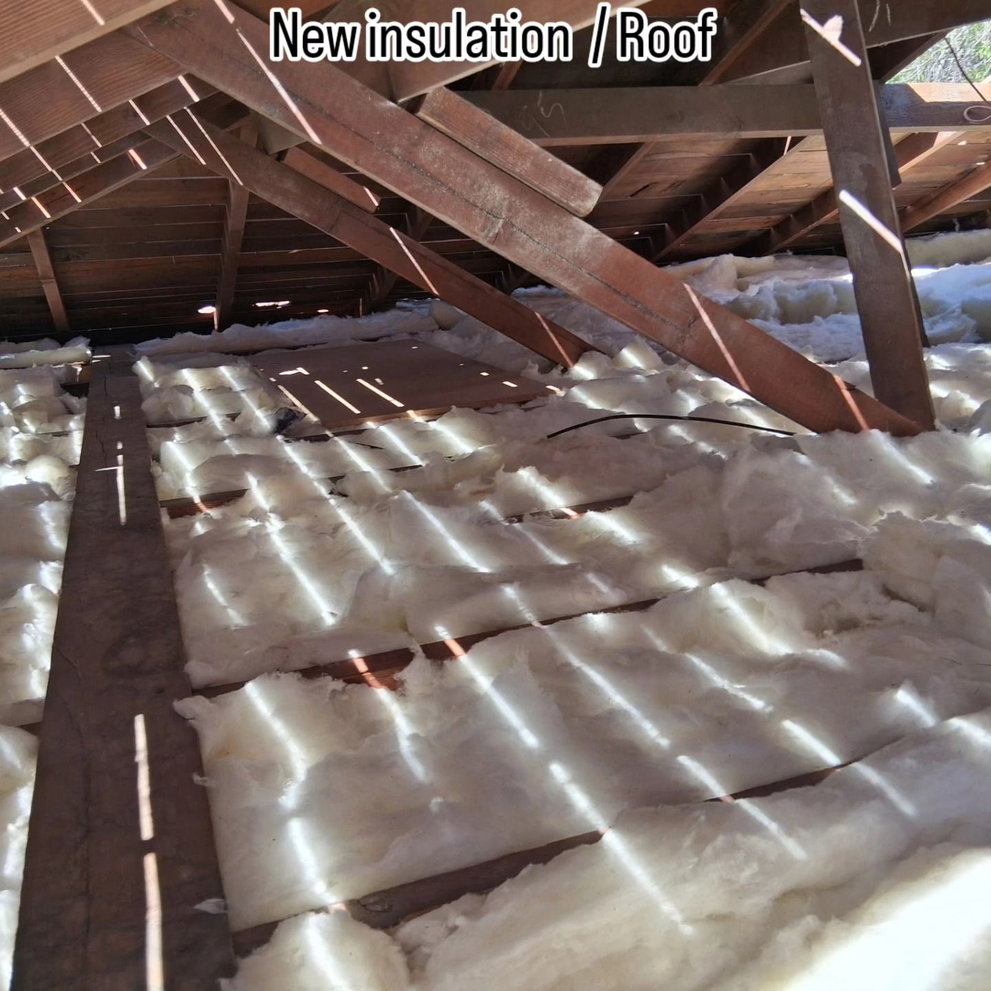 Attic with new white insulation laid between roof rafters and beams