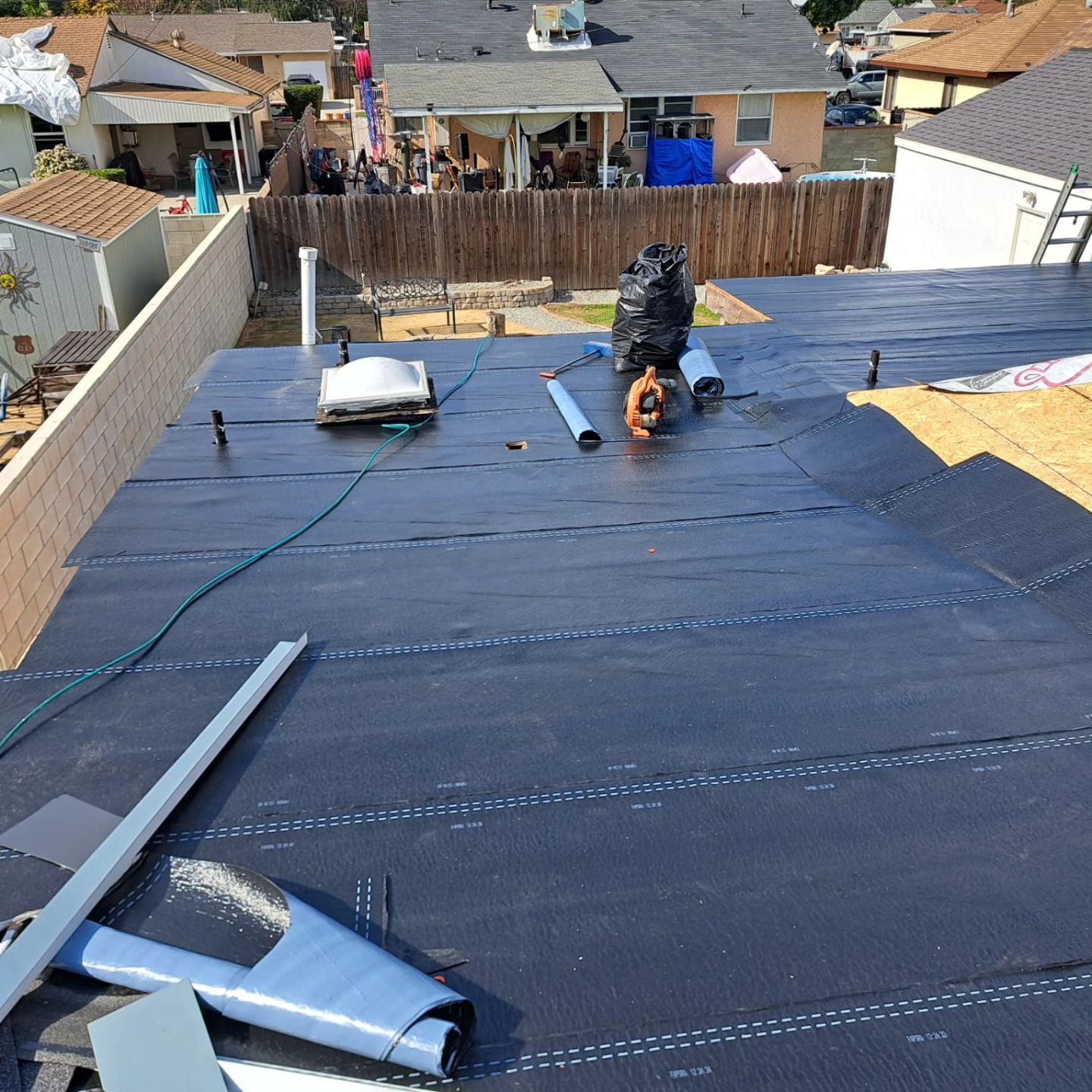 Roofers installing black underlayment on a sloped roof with tools and materials scattered nearby.