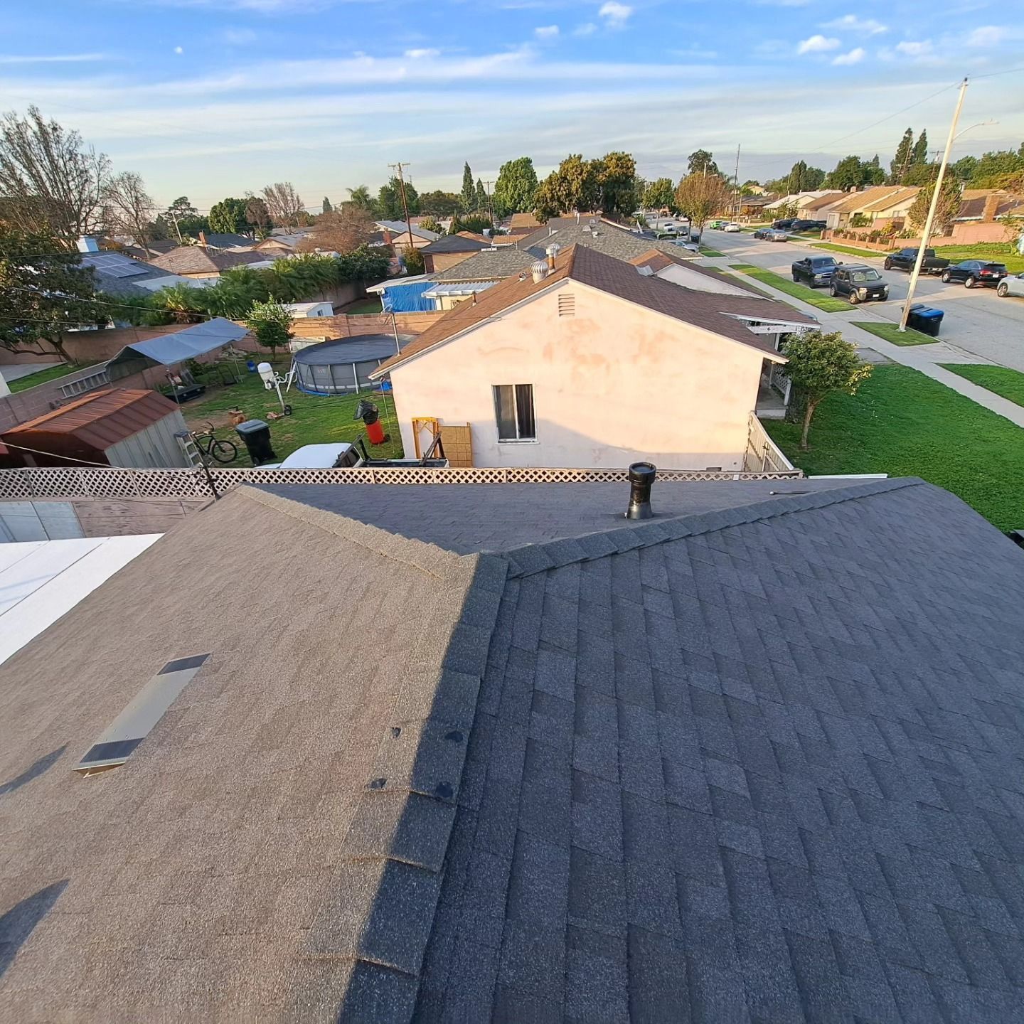 View from a rooftop over suburban houses and streets at sunset, with two workers on the roof.