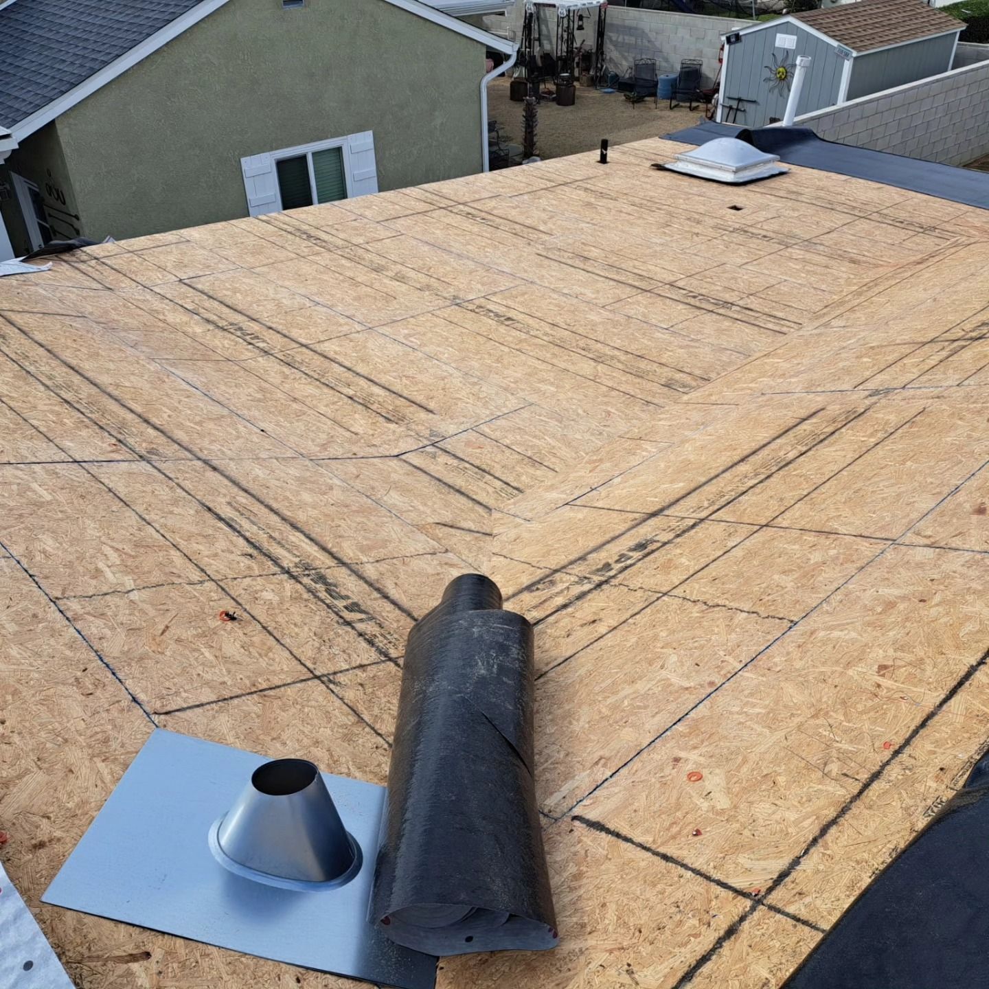 Roof under construction with exposed plywood, roof vents, and roofing lines marked across the surface