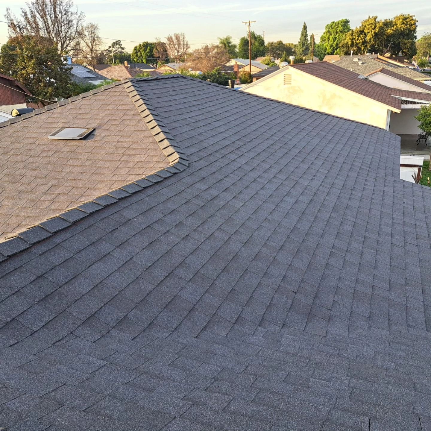 Residential rooftops with gray shingles in a suburban neighborhood at sunset