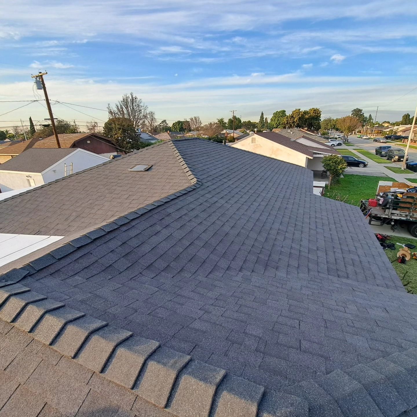 Residential neighborhood with a newly shingled dark gray roof under a blue sky