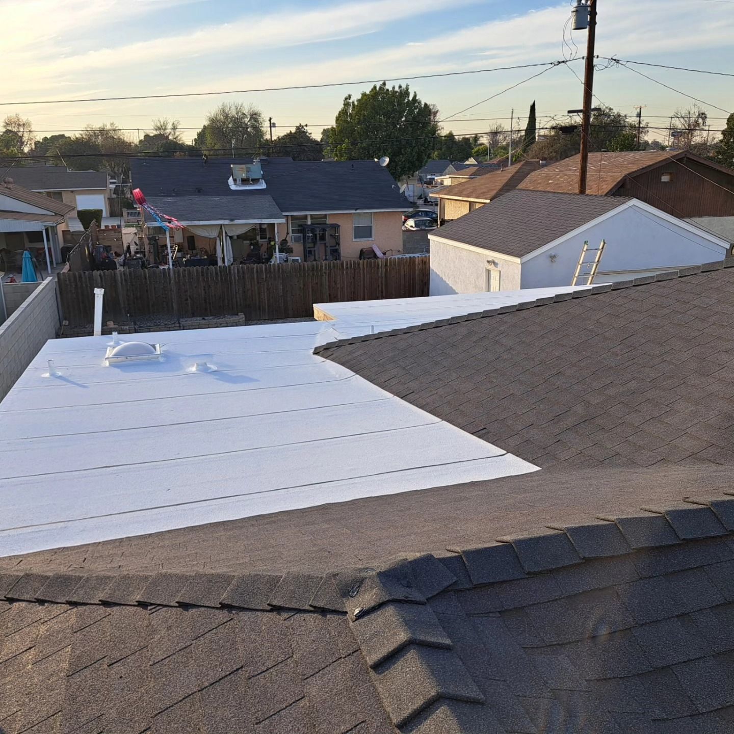 Roof under repair with white underlayment exposed beside brown shingles in a suburban neighborhood