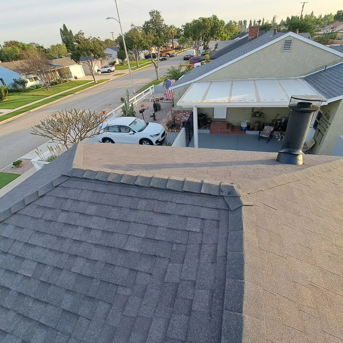 View from a rooftop over a suburban street, driveway with white car, and a house with a covered patio