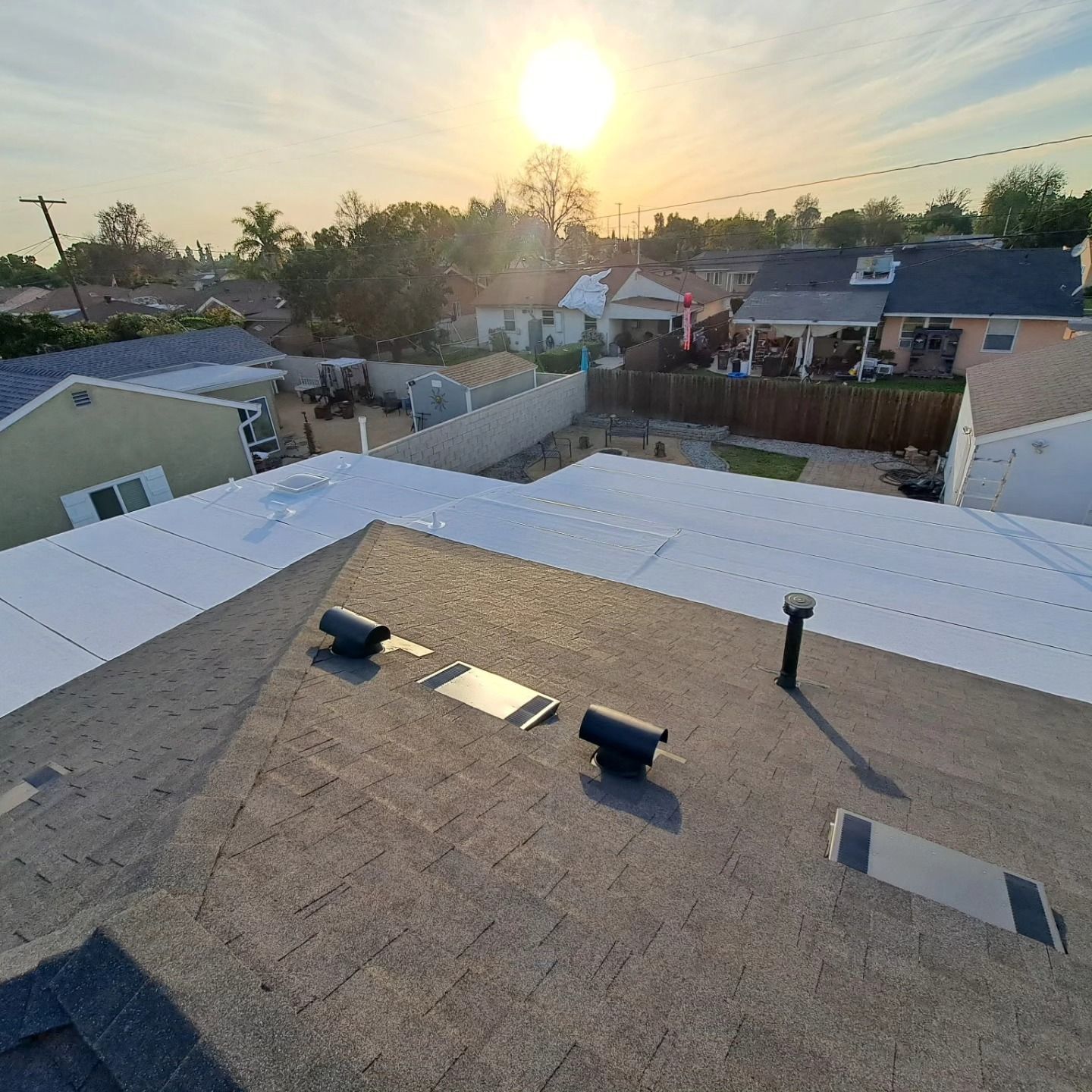 Sunset over a suburban neighborhood, seen from a rooftop with vents and a skylight.