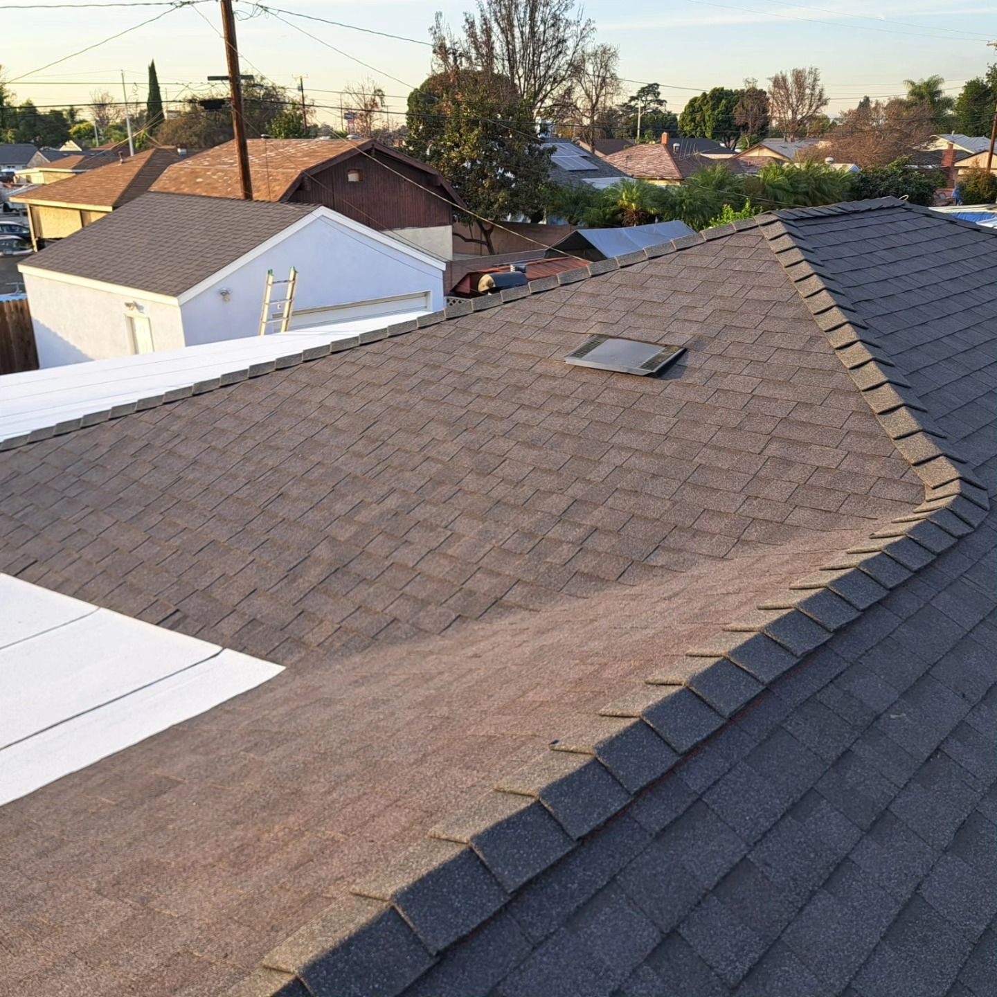 Rooftop with brown shingles and a skylight overlooking neighboring houses at sunset