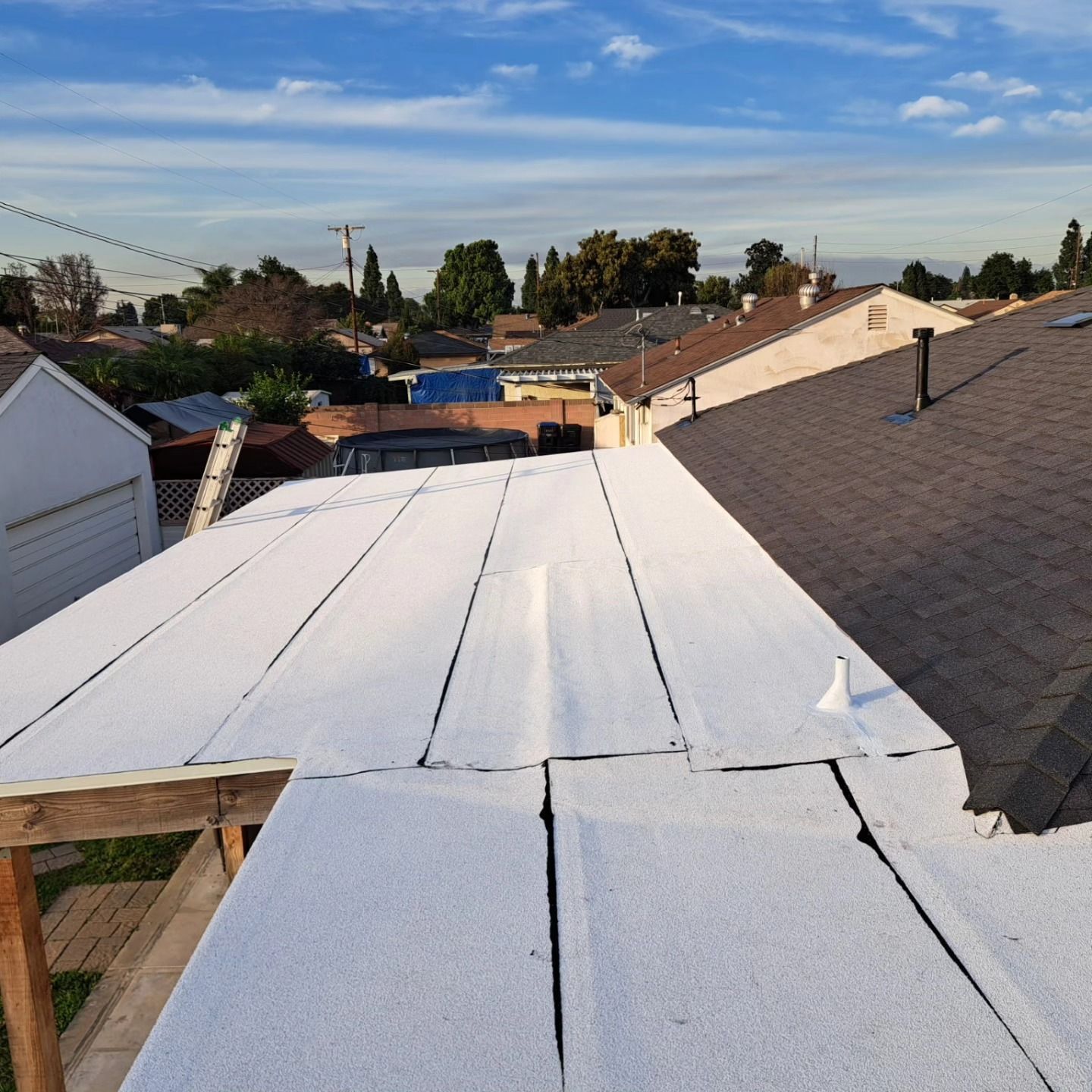 Partially repaired roof with white underlayment beside a gray shingle roof under a blue sky
