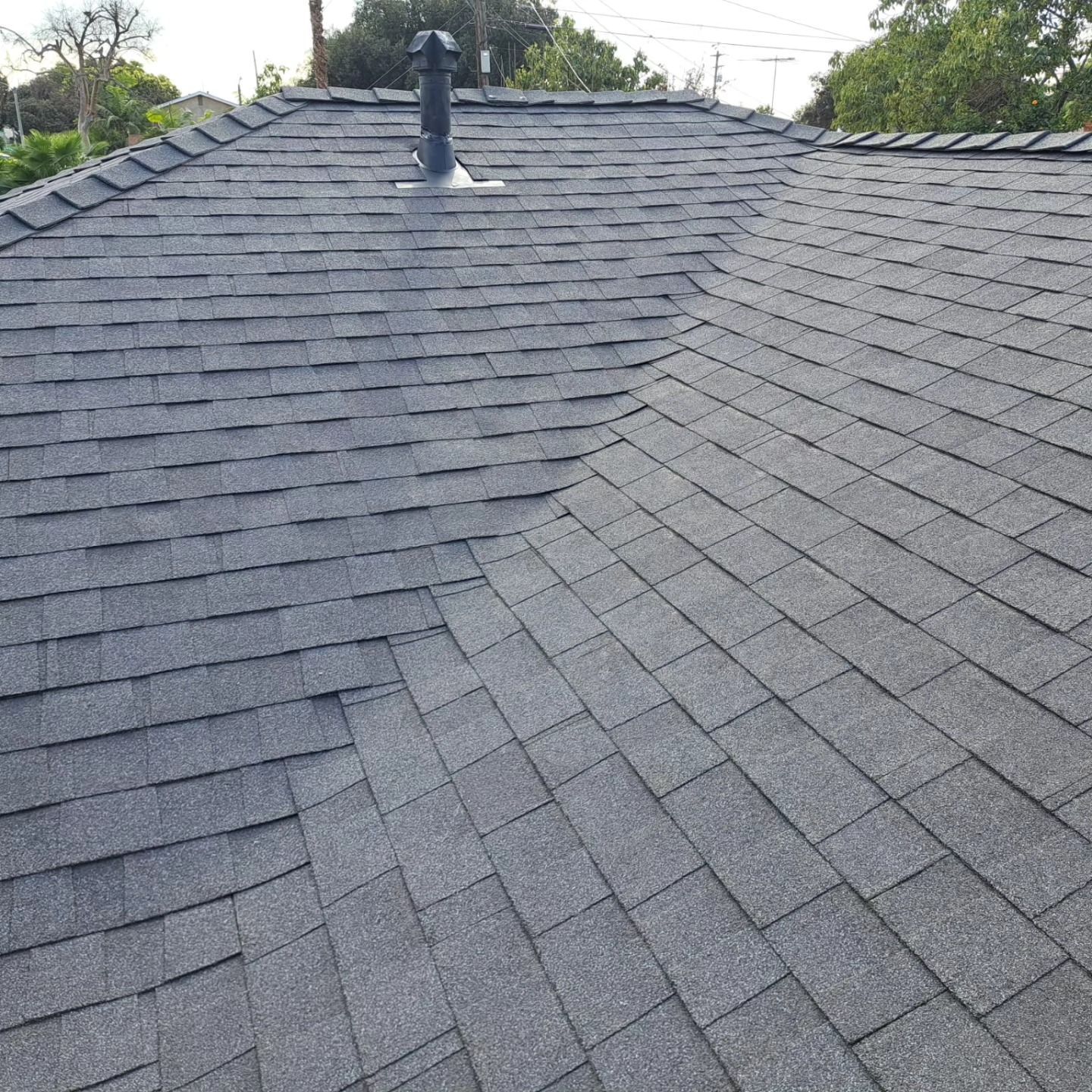 Gray shingled roof with a chimney and visible ridgelines under a cloudy sky