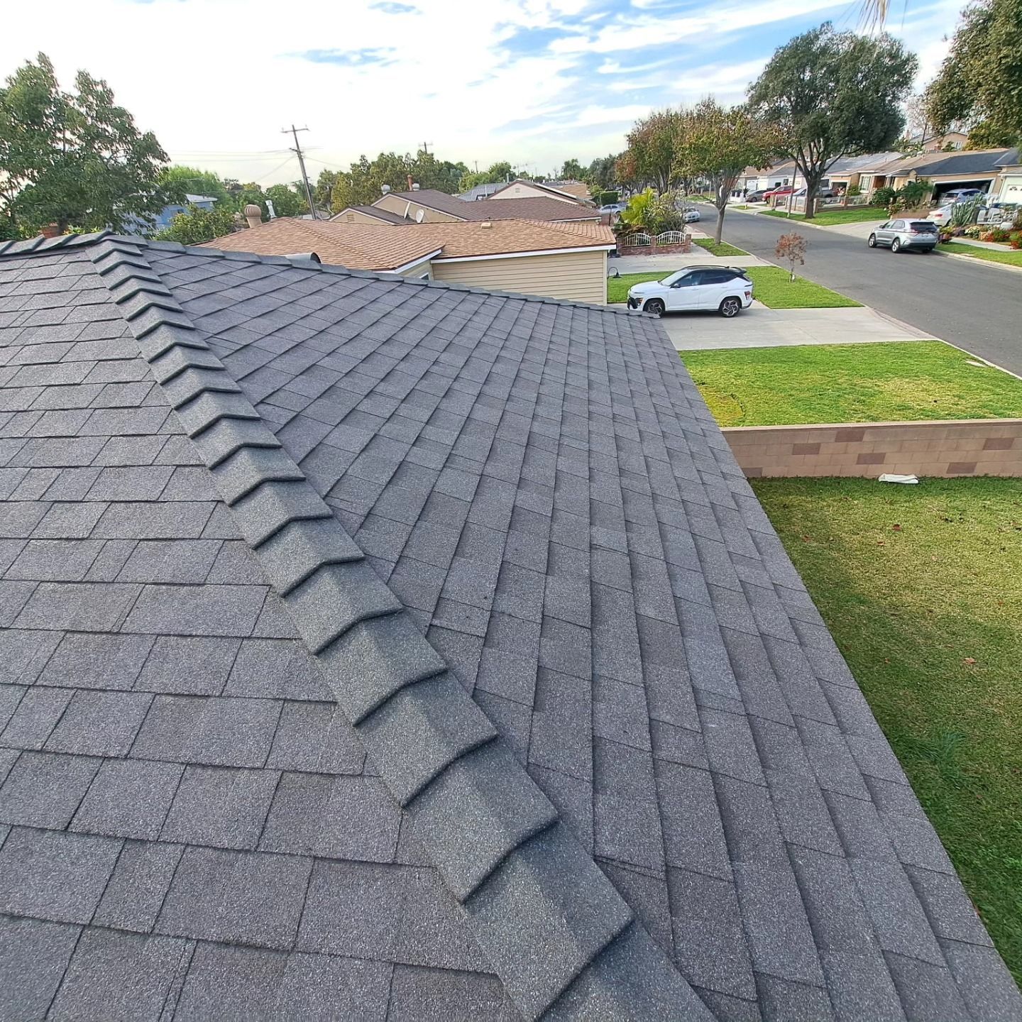 New gray shingle roof on a suburban house, viewed from above with neighborhood homes in the background