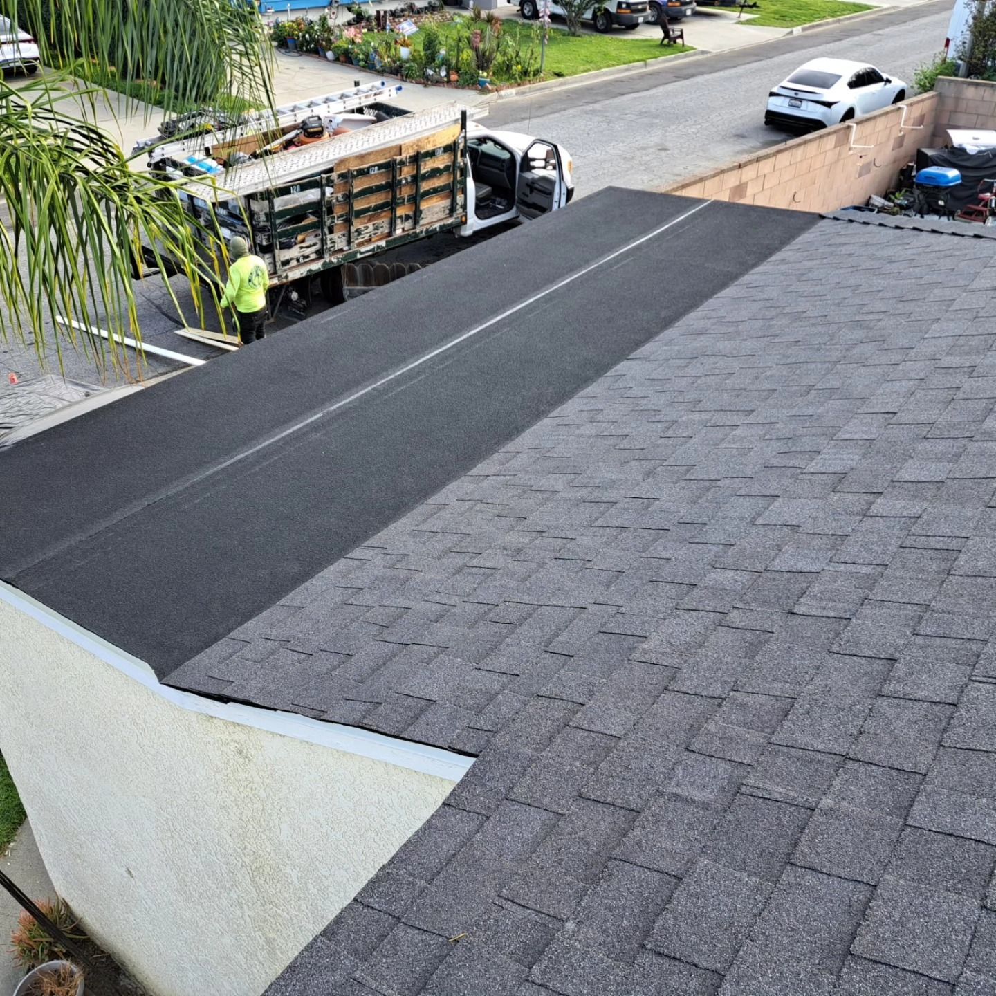 Roof being repaired with fresh black shingles beside a parked work truck on a street.