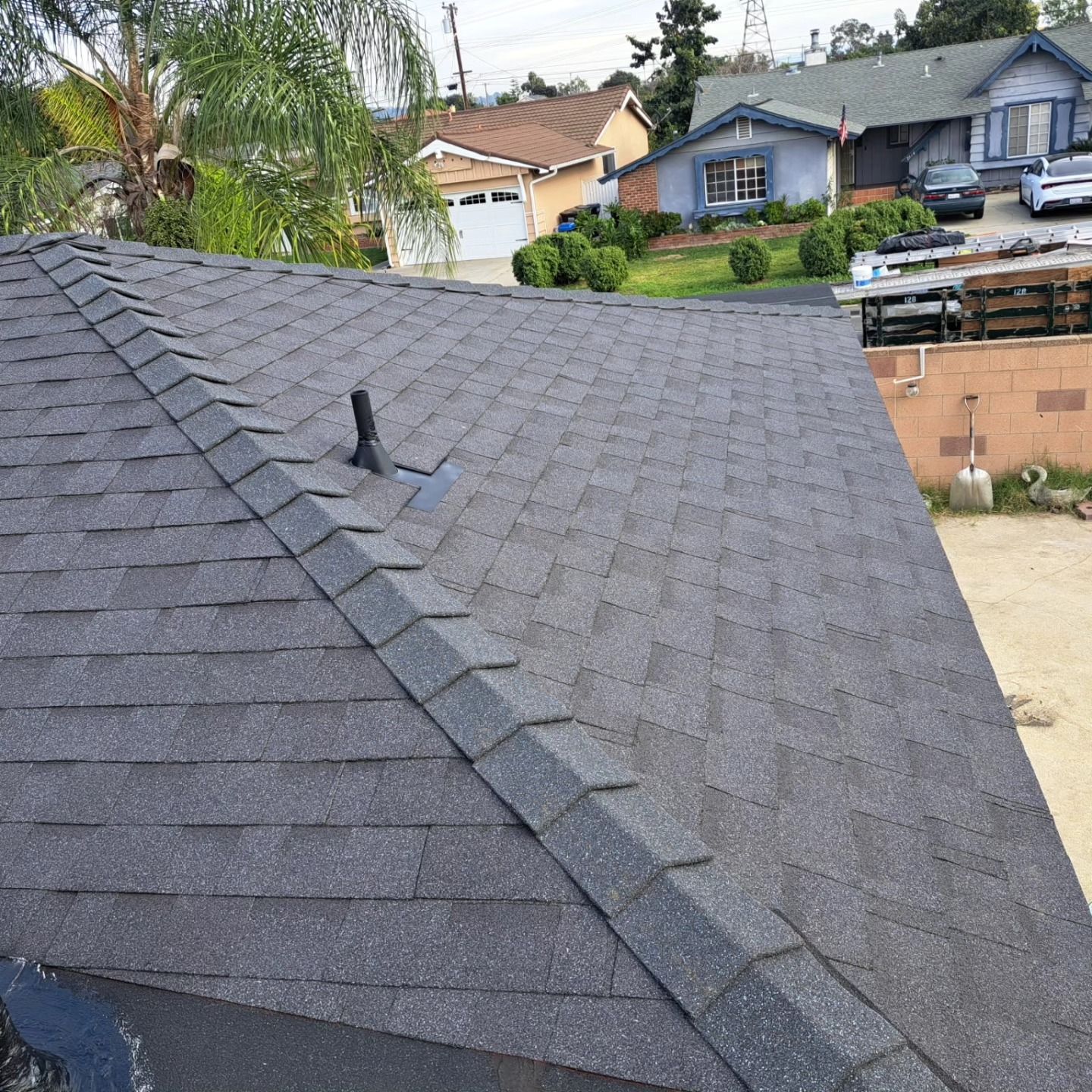 Dark gray shingled roof with a vent, viewed from above with houses in the background