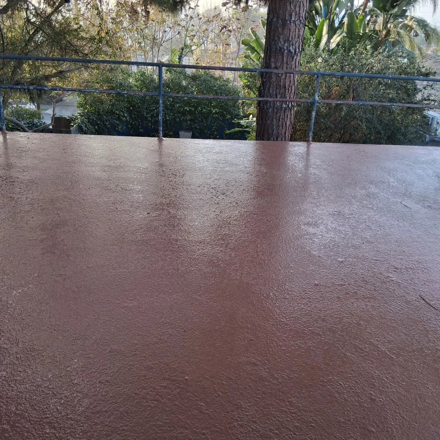 Wet brown patio surface with a railing and trees in the background
