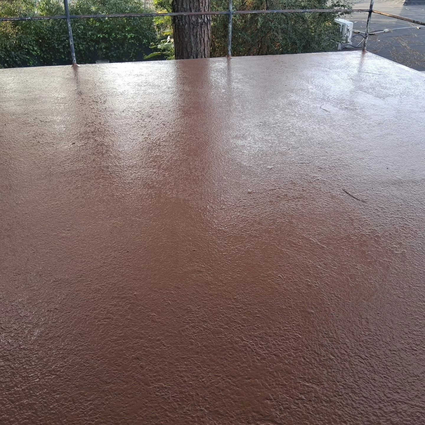 Wet brown patio surface with rain droplets, viewed behind a metal fence.