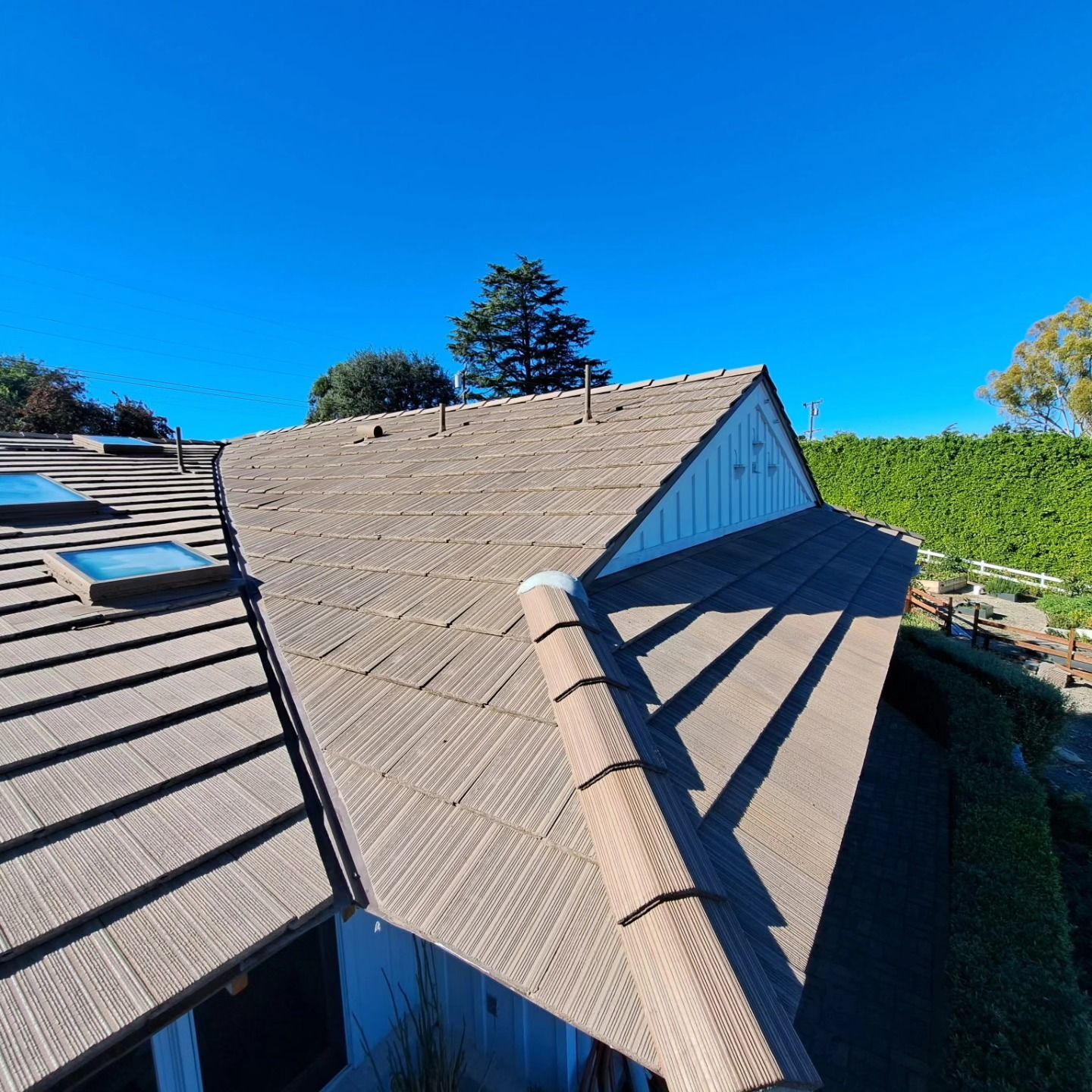 Rooftops with tan shingles under a bright blue sky, viewed from above.