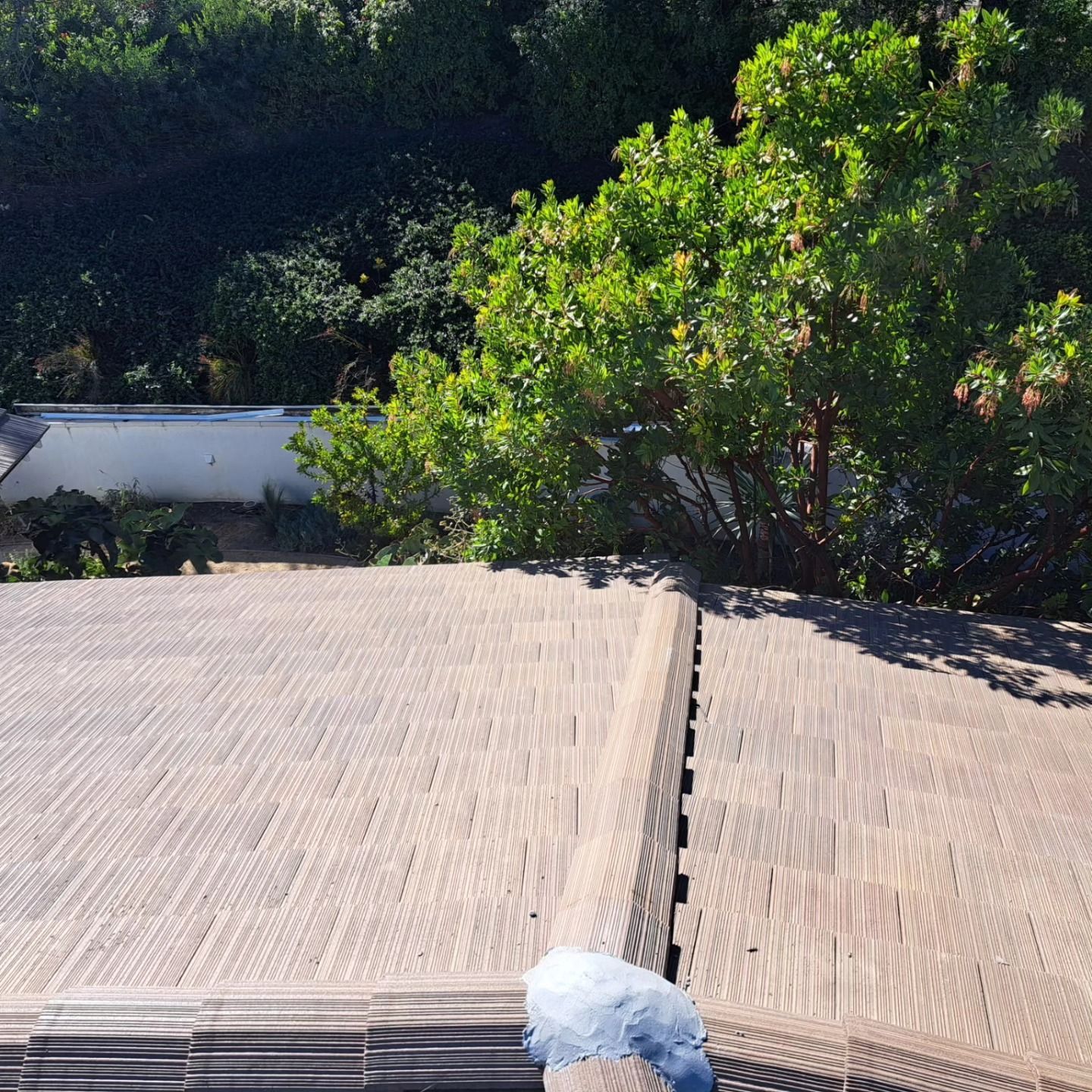 Woven mat rooftop with a small white object at the edge, backed by green trees and a white wall