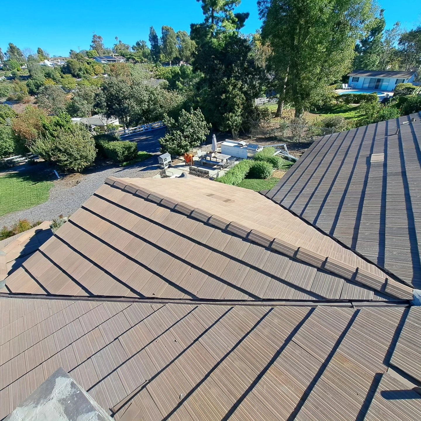Rooftop with tan shingles overlooking a backyard with trees, gravel, and a blue sky
