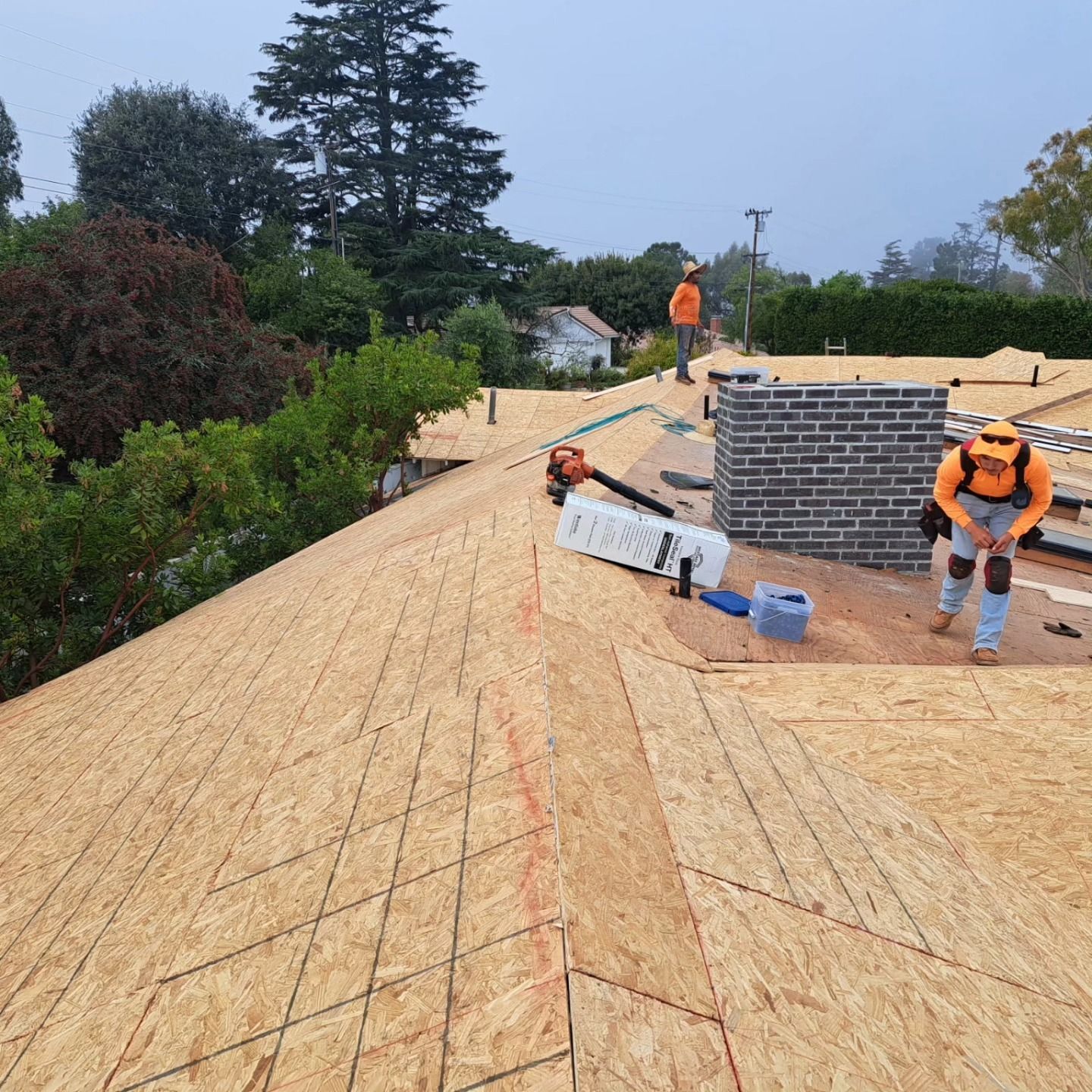 Workers installing plywood roofing on a house under construction, with tools and materials on the roof.