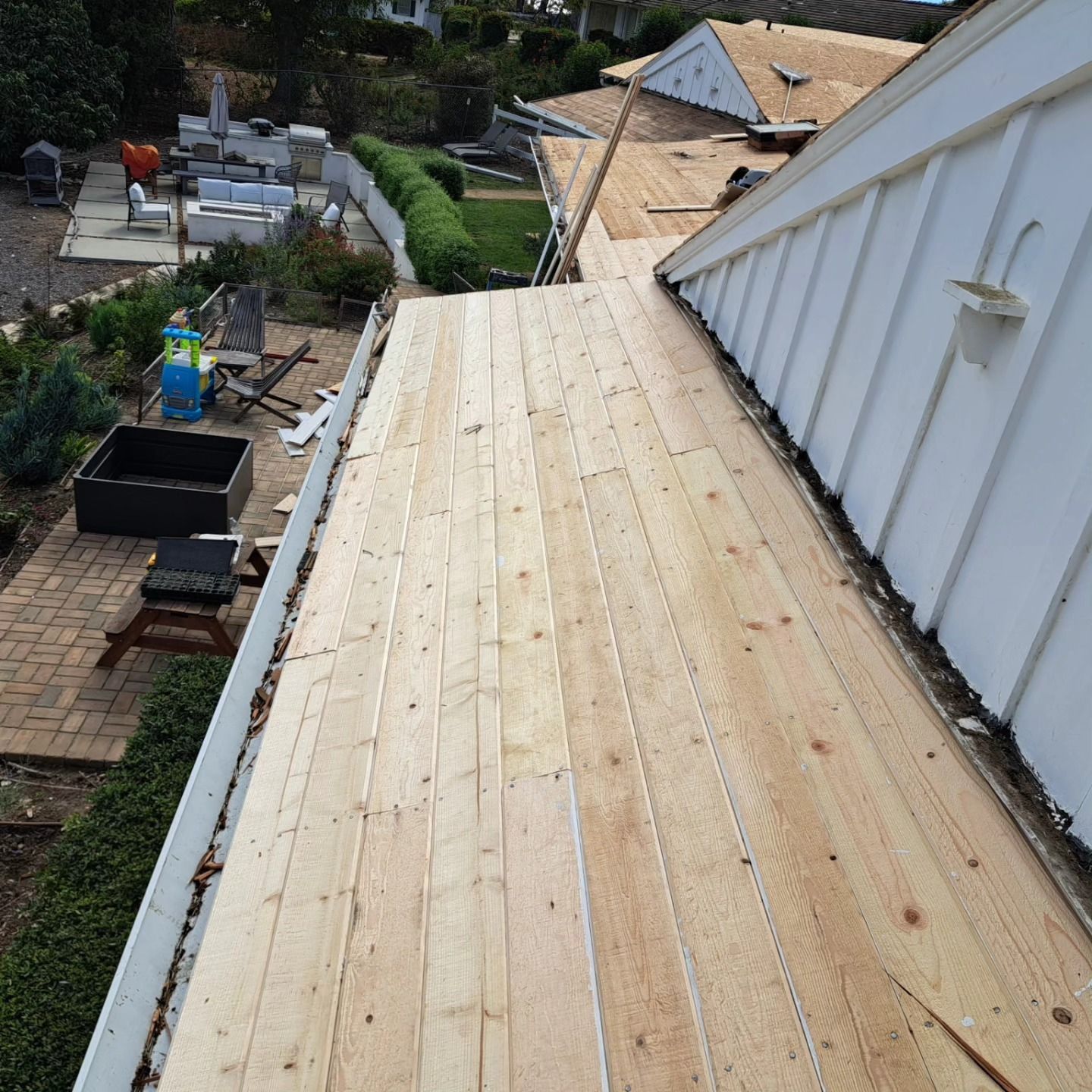 Freshly installed wooden roof deck beside a white house, overlooking a yard and rooftops below.