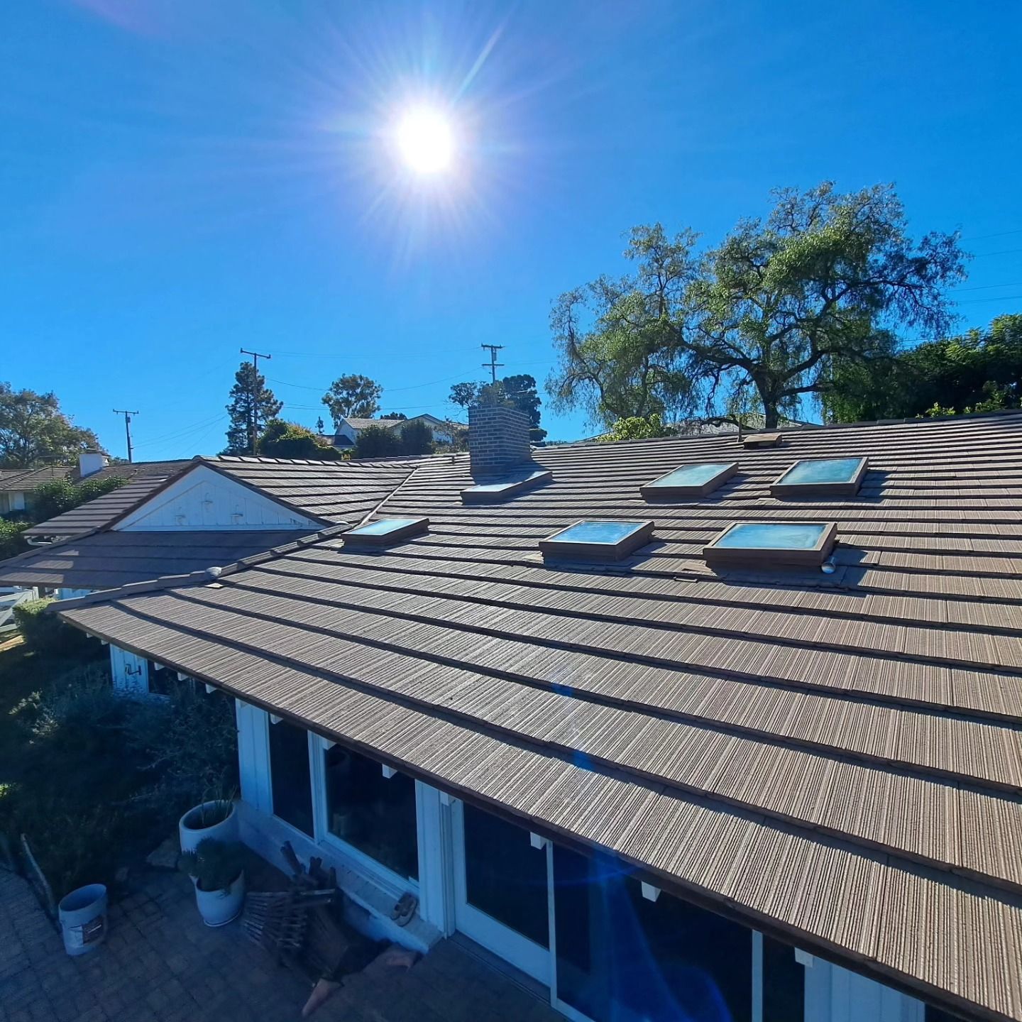 Sunlit rooftop with skylights, chimney, and solar panels under a clear blue sky