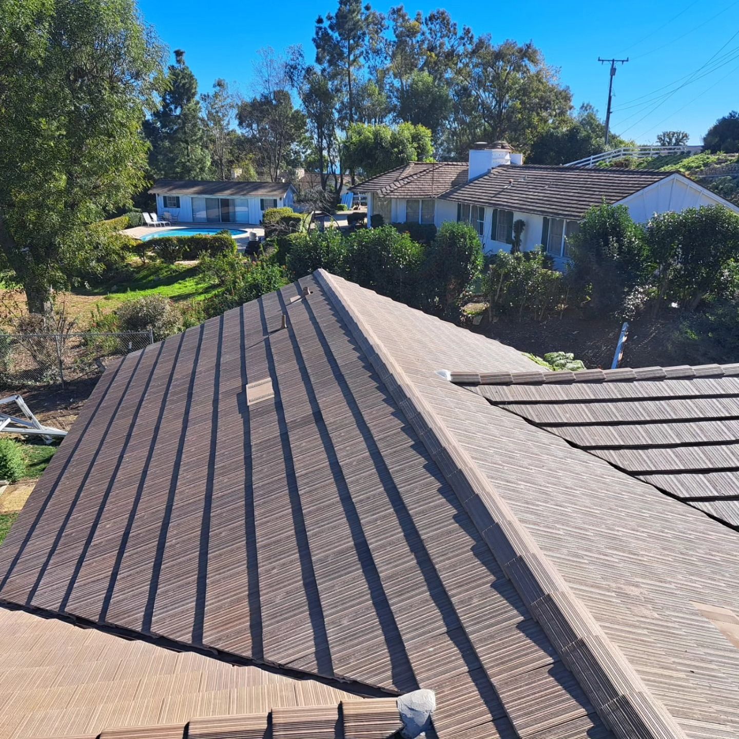 Roof view with brown shingles and nearby houses under a clear blue sky