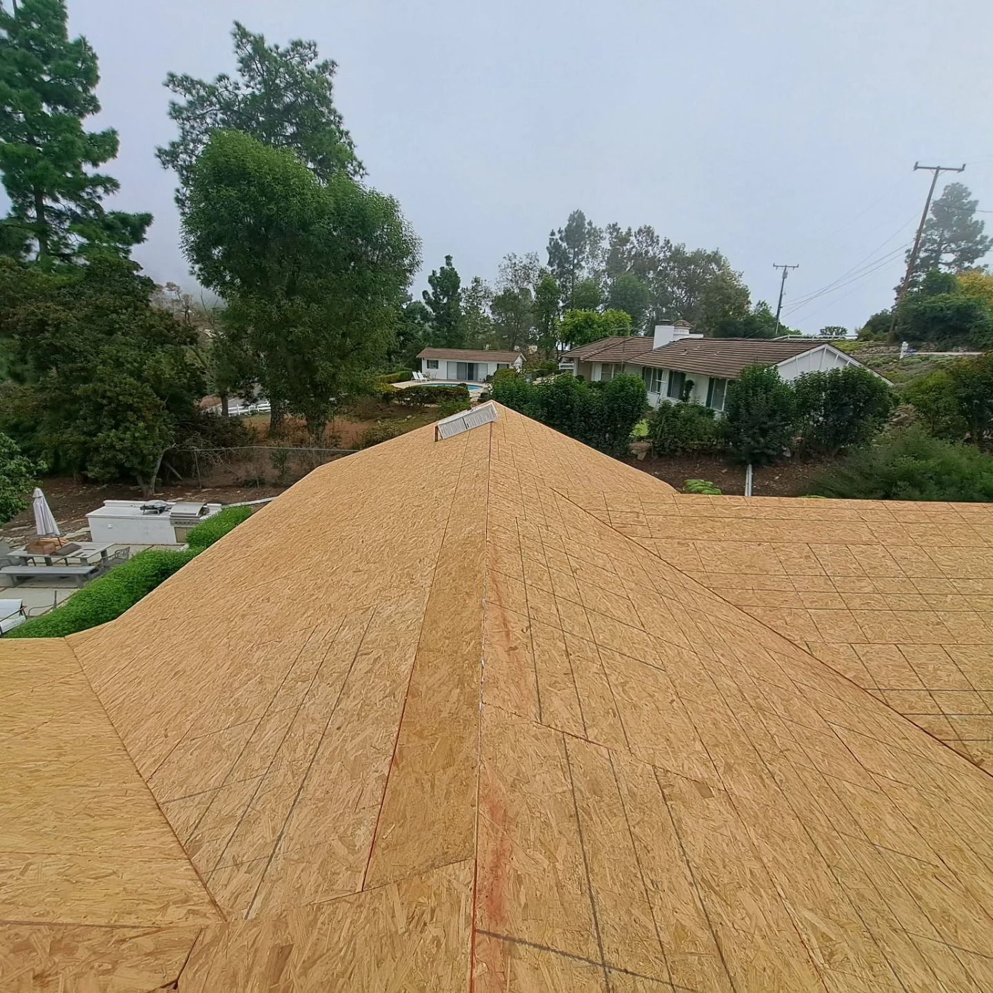 Tan wooden roof under construction, viewed from above, with trees and houses in the background.
