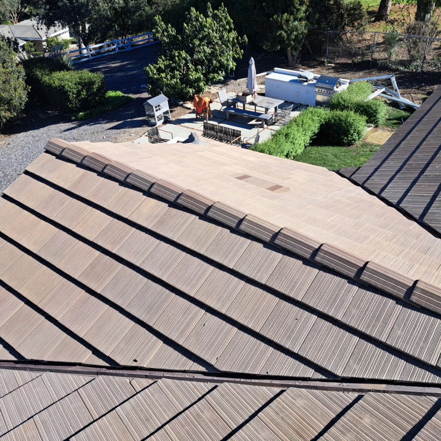 Close-up of a tan shingle roof with rooftop vents and a backyard visible beyond