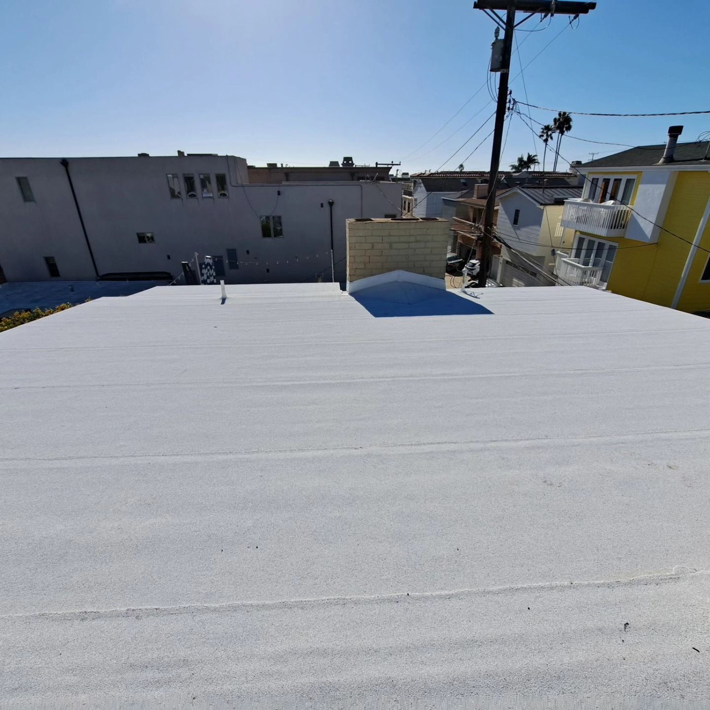White flat rooftop with neighboring houses, utility pole, and blue sky in the background