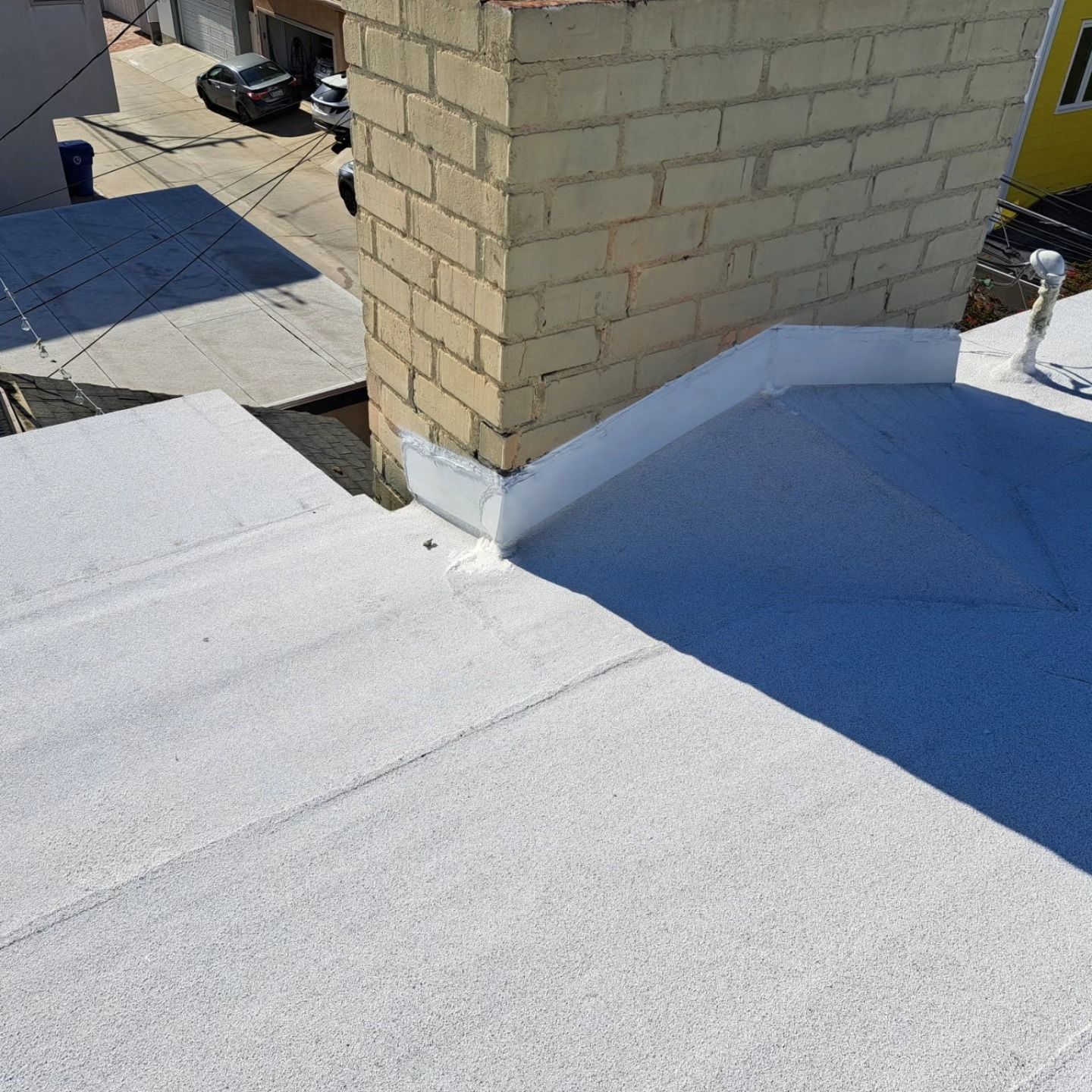 White rooftop with a tan brick chimney and blue shadow near a roof edge