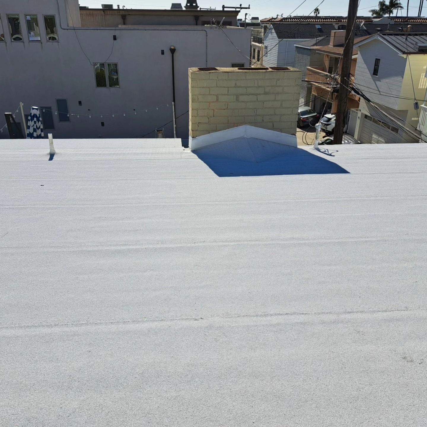 Rooftop with white coating, small blue section, and neighboring buildings under bright sunlight