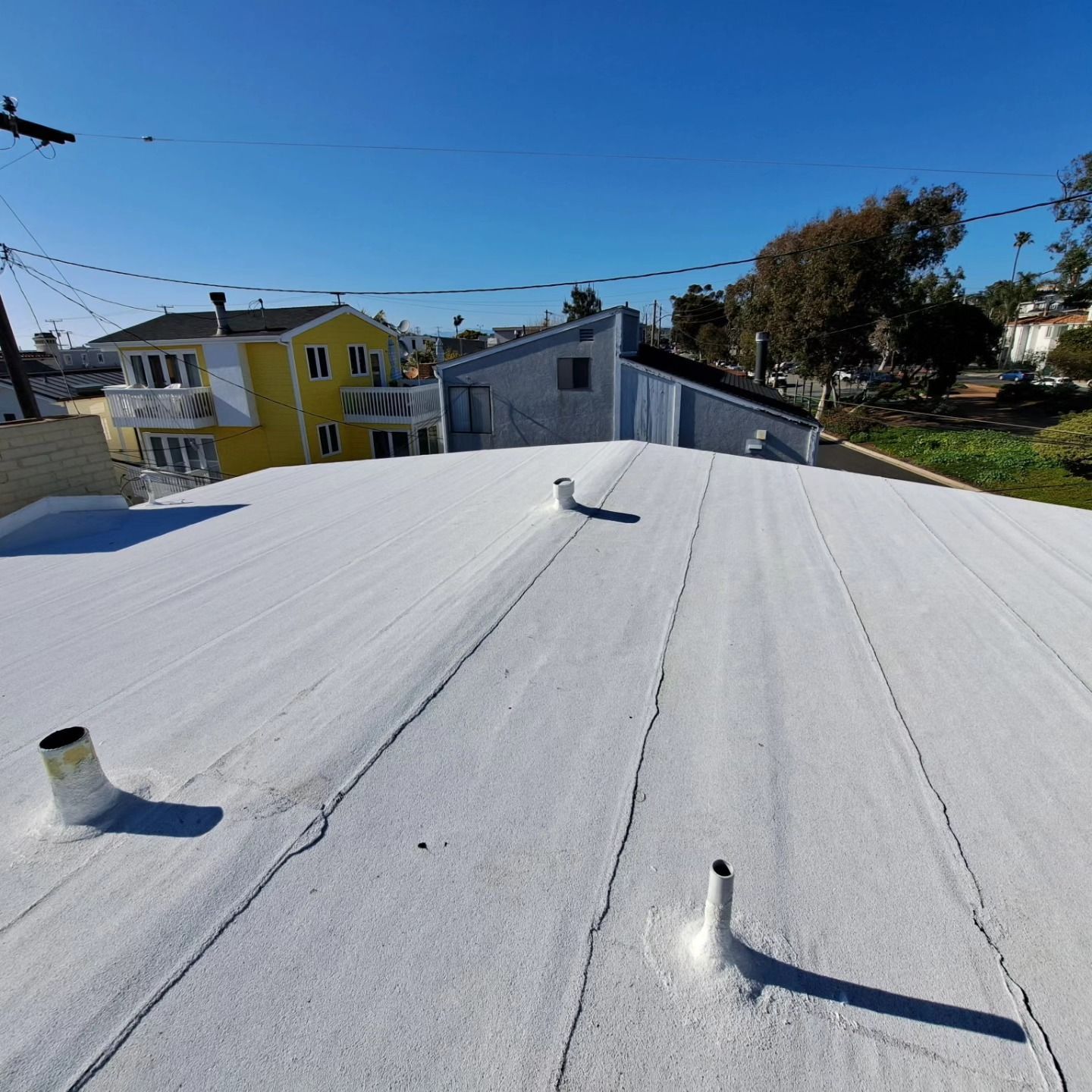 White rooftop with vents overlooking neighboring houses under a clear blue sky.