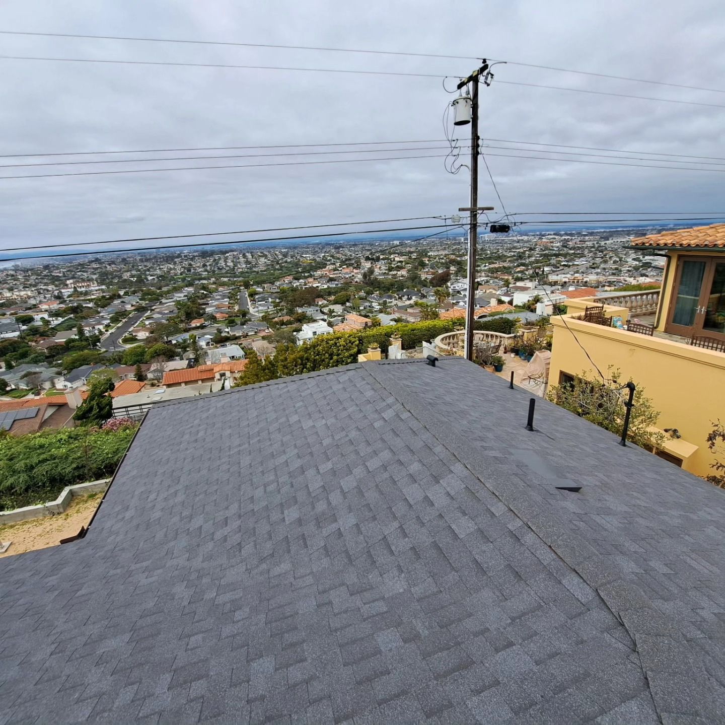 Rooftop view over a coastal neighborhood with gray shingles, power lines, and cloudy sky.