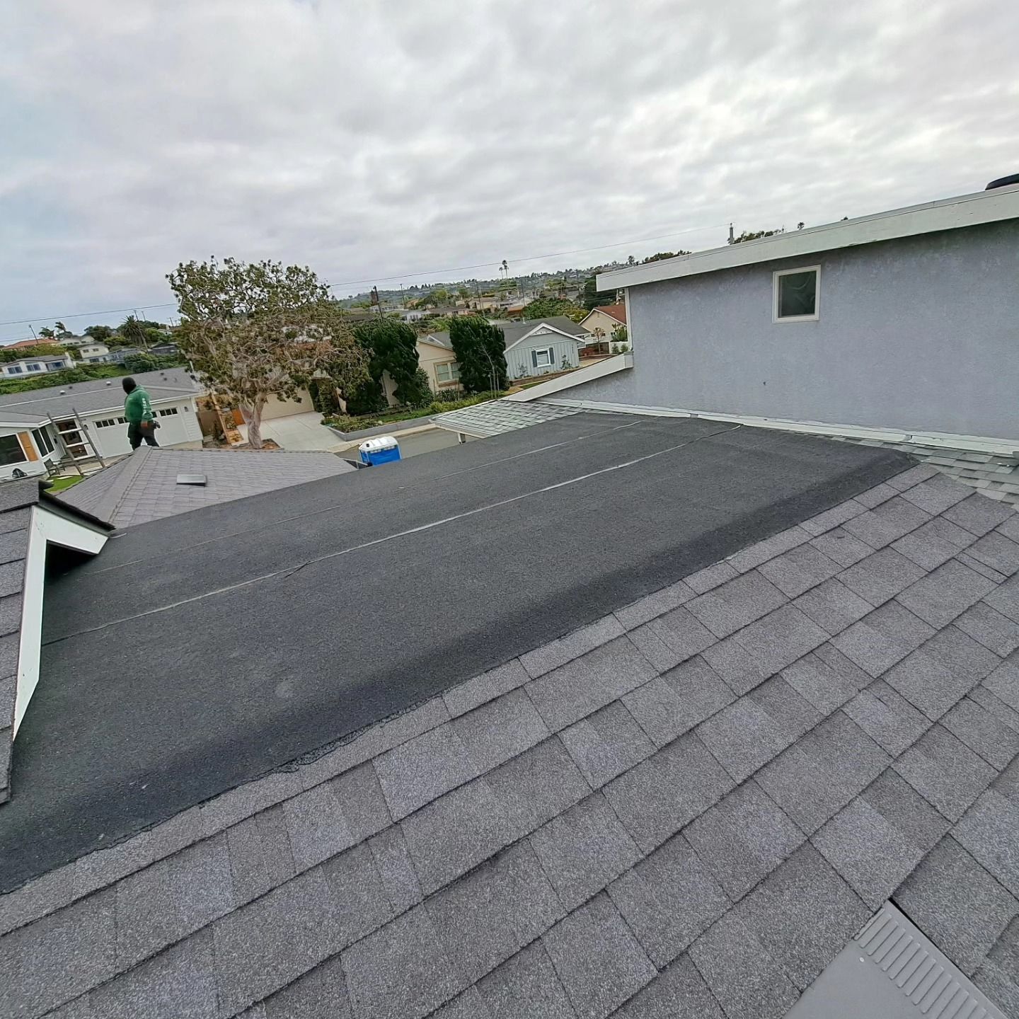 Gray shingled rooftop with a distant neighborhood view under a cloudy sky